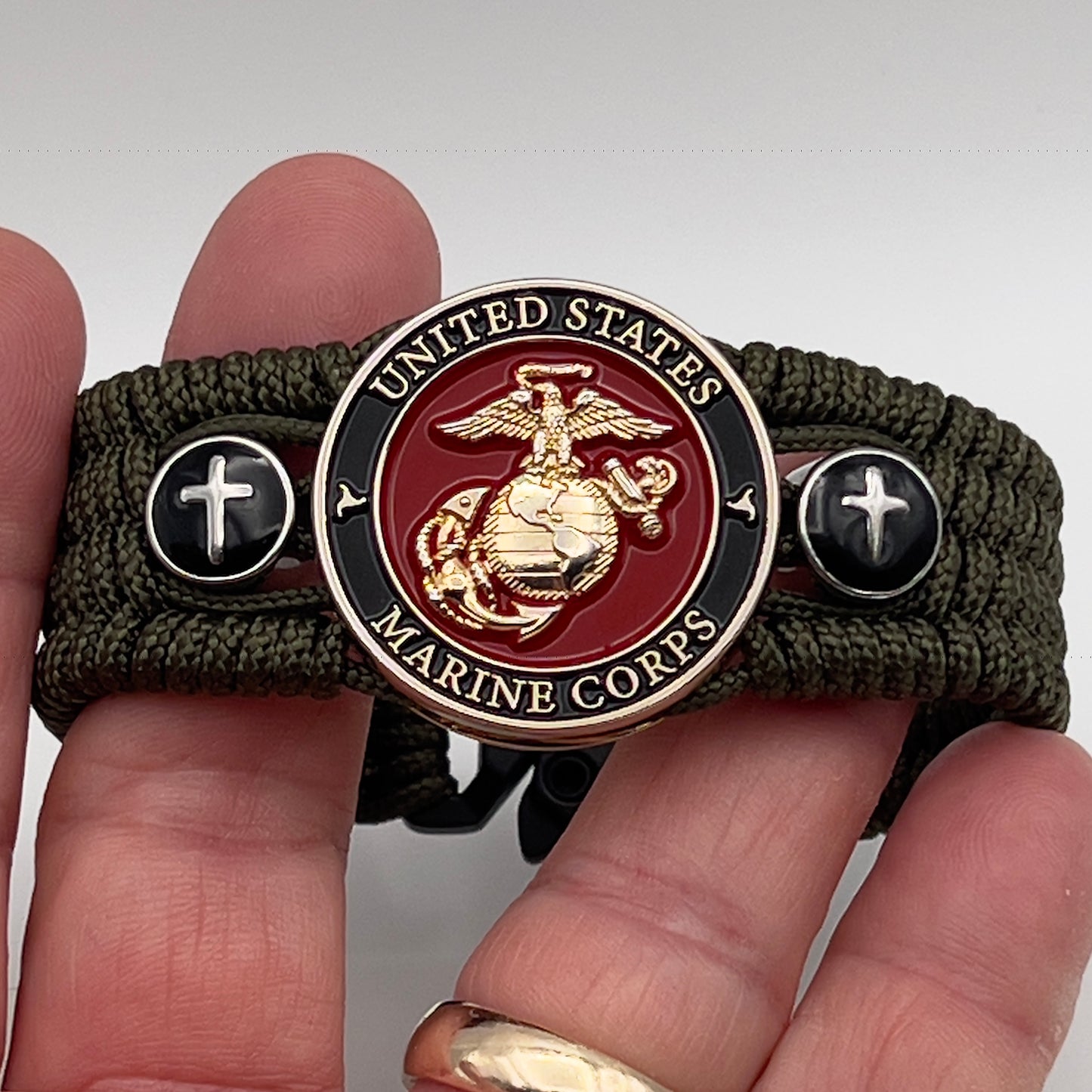 Thin, medium width, flexible and comfortable braided United States Marine Corps bracelet featuring a 24K gold plated USMC officer Eagle Globe and Anchor medallion, two Christian crosses, a black Cobra style tactical buckle and woven with Olive Drab Type-1 paracord.