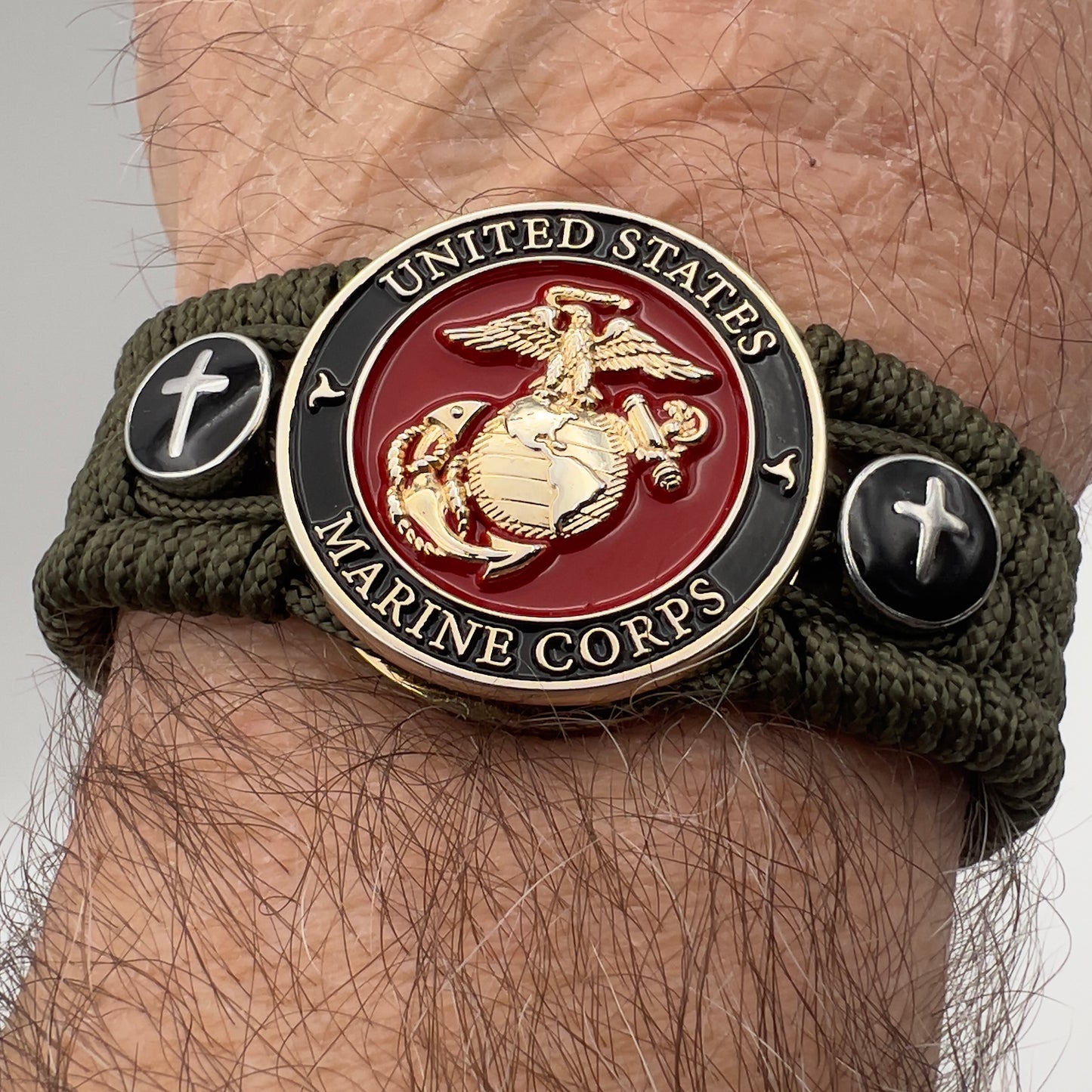 Thin, medium width, flexible and comfortable braided United States Marine Corps bracelet featuring a 24K gold plated USMC officer Eagle Globe and Anchor medallion, two Christian crosses, a black Cobra style tactical buckle and woven with Olive Drab Type-1 paracord.