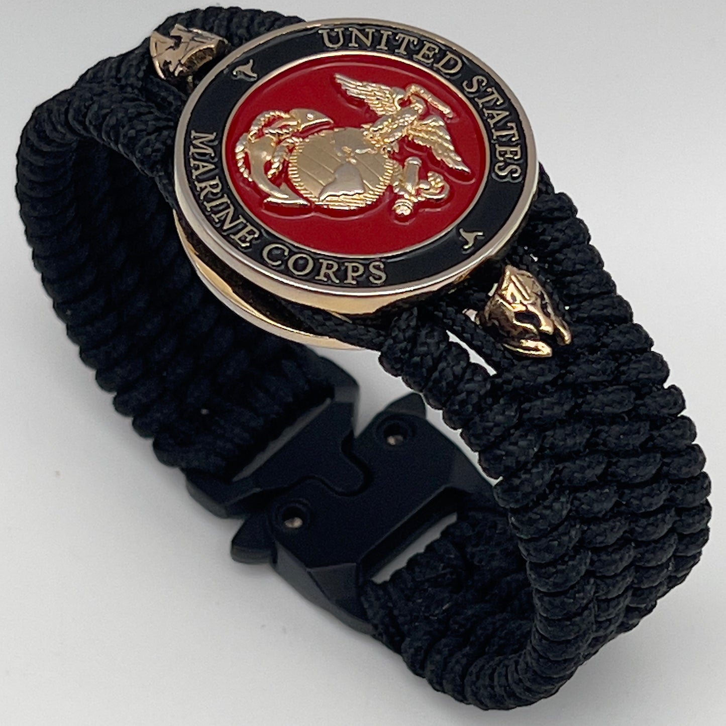 Thin, medium width, flexible and comfortable braided United States Marine Corps bracelet featuring a 24K gold plated USMC officer Eagle Globe and Anchor medallion, two brass Spartan helmets, a black Cobra style tactical buckle and woven with black Type-1 paracord.