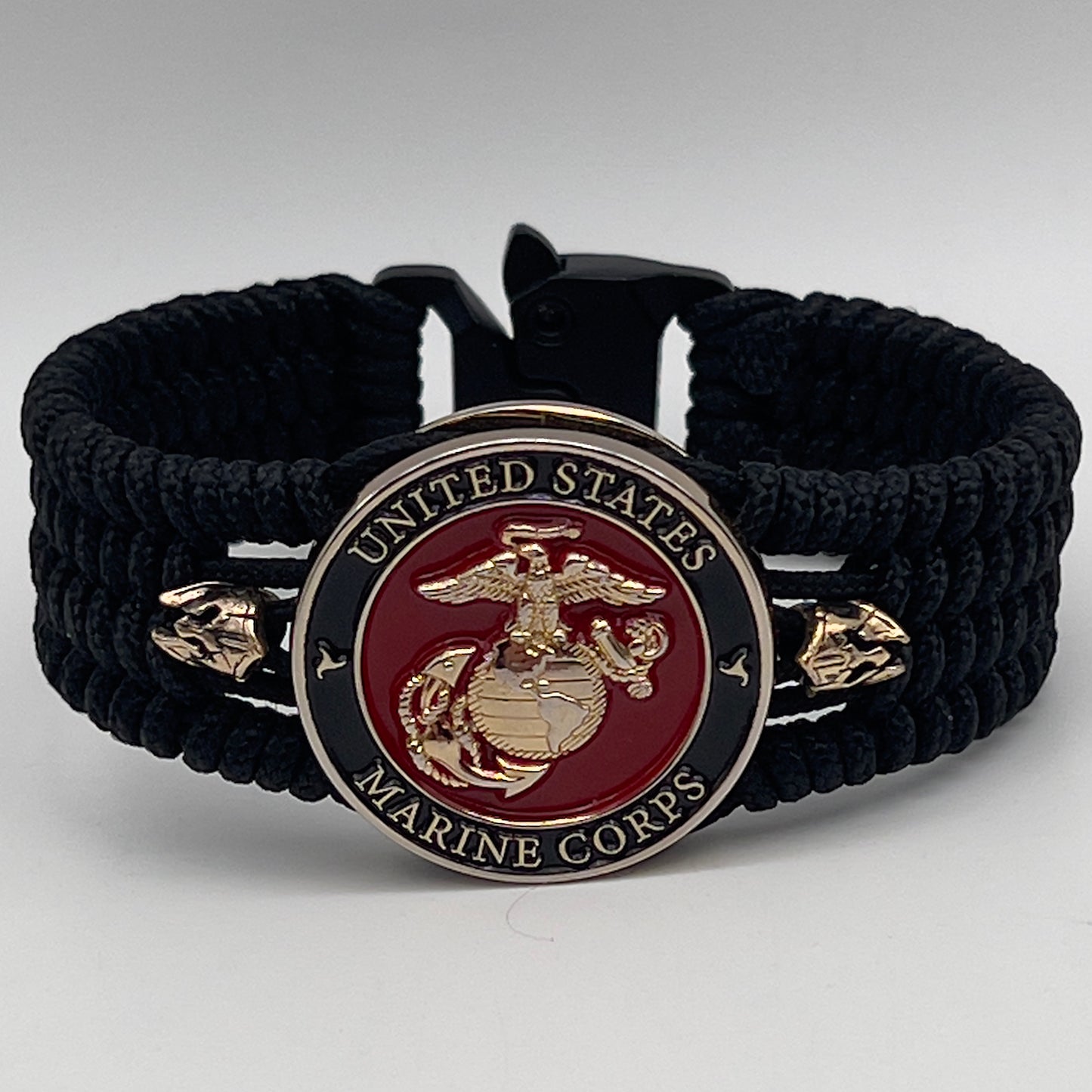 Thin, medium width, flexible and comfortable braided United States Marine Corps bracelet featuring a 24K gold plated USMC officer Eagle Globe and Anchor medallion, two brass Spartan helmets, a black Cobra style tactical buckle and woven with black Type-1 paracord.