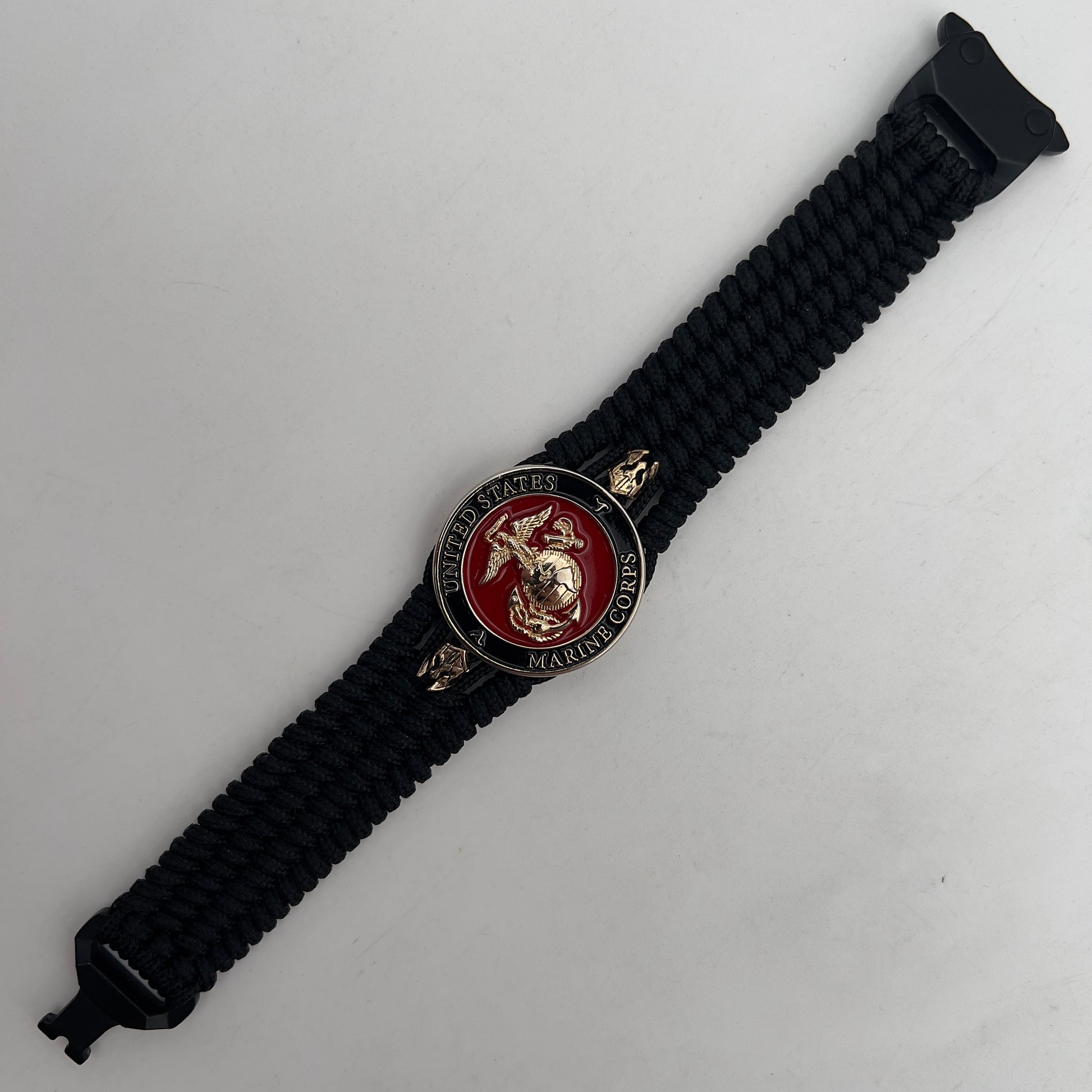 Thin, medium width, flexible and comfortable braided United States Marine Corps bracelet featuring a 24K gold plated USMC officer Eagle Globe and Anchor medallion, two brass Spartan helmets, a black Cobra style tactical buckle and woven with black Type-1 paracord.
