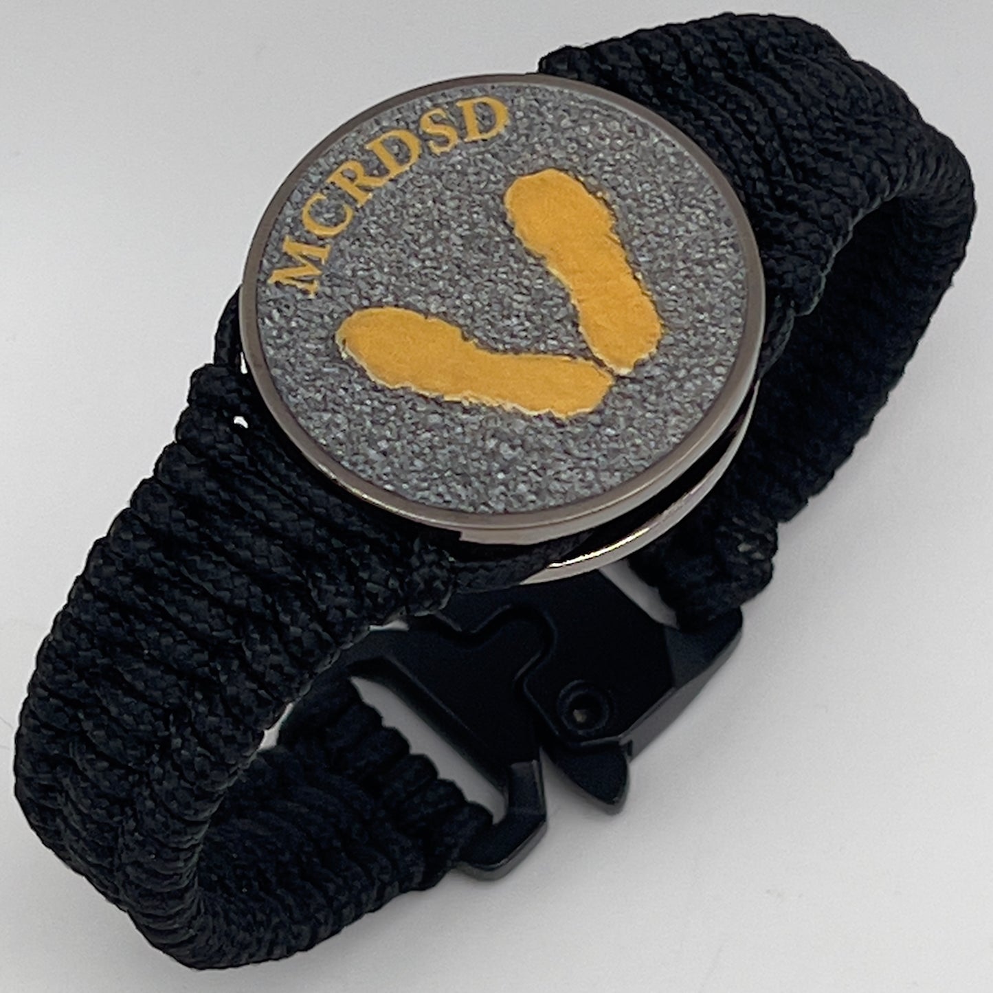 Thin, narrow, flexible and comfortable braided United States Marine Corps Recruit Depot Yellow Footprints bracelet featuring a black nickel plated UV enamel painted medallion replica of an actual set of USMC footprints, a black Cobra style tactical buckle and woven with black Type-1 paracord.