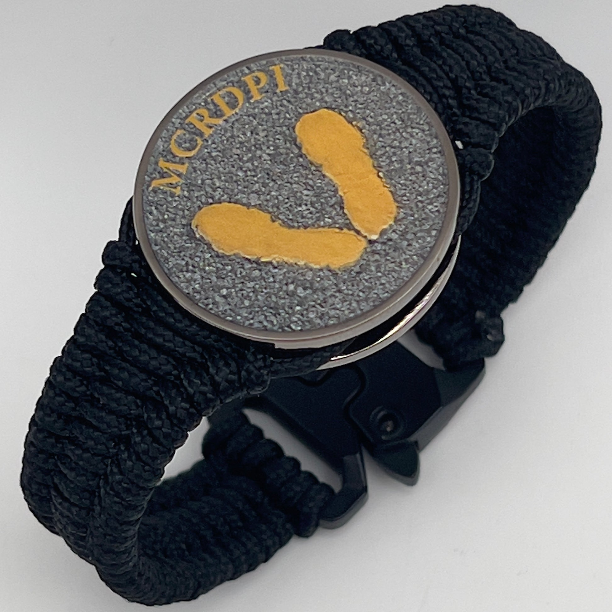 Thin, narrow, flexible and comfortable braided United States Marine Corps Recruit Depot Yellow Footprints bracelet featuring a black nickel plated UV enamel painted medallion replica of an actual set of USMC footprints, a black Cobra style tactical buckle and woven with black Type-1 paracord.