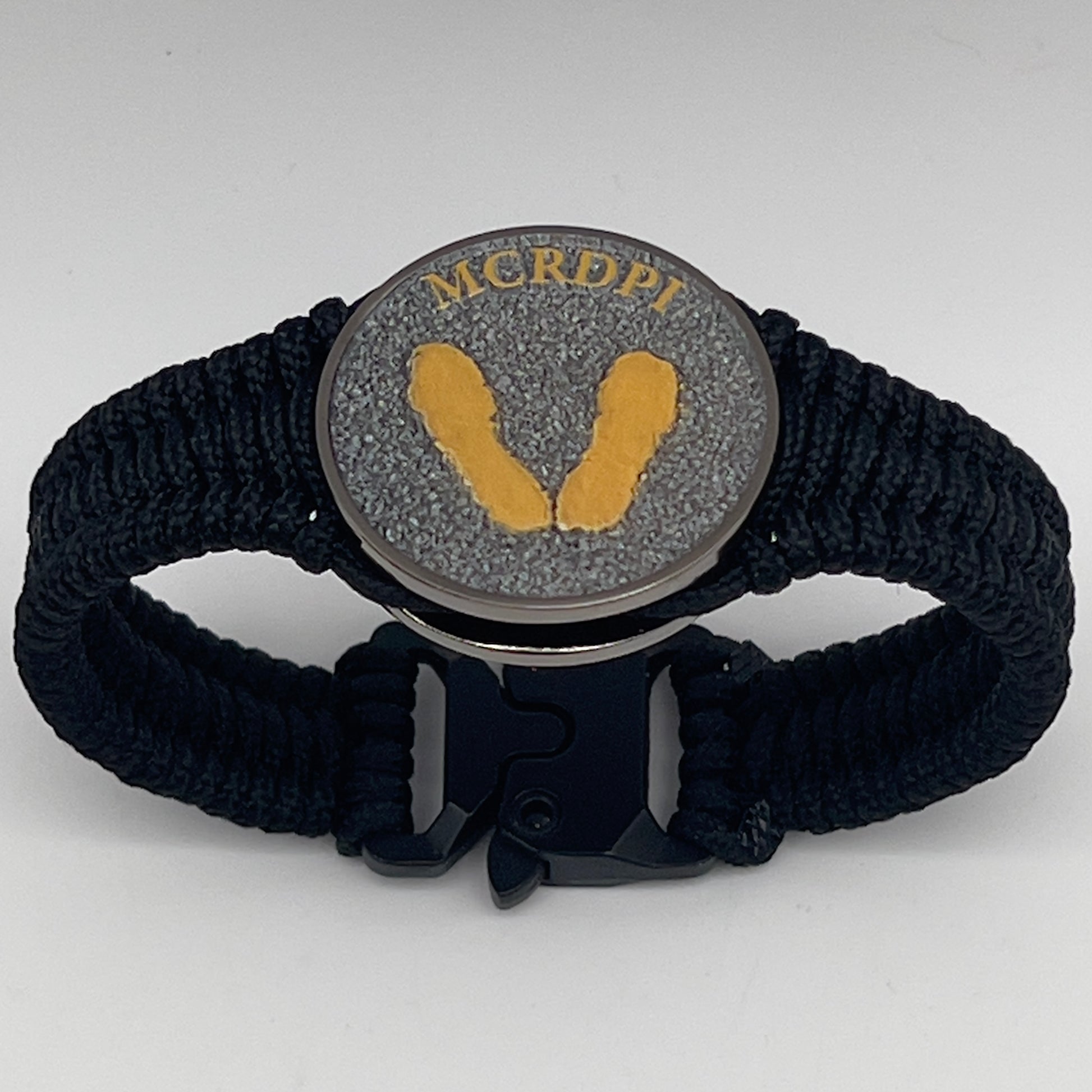 Thin, narrow, flexible and comfortable braided United States Marine Corps Recruit Depot Yellow Footprints bracelet featuring a black nickel plated UV enamel painted medallion replica of an actual set of USMC footprints, a black Cobra style tactical buckle and woven with black Type-1 paracord.