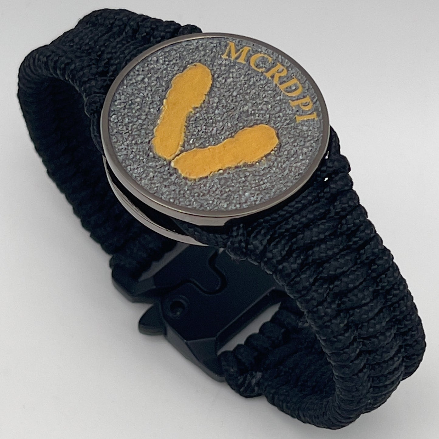Thin, narrow, flexible and comfortable braided United States Marine Corps Recruit Depot Yellow Footprints bracelet featuring a black nickel plated UV enamel painted medallion replica of an actual set of USMC footprints, a black Cobra style tactical buckle and woven with black Type-1 paracord.