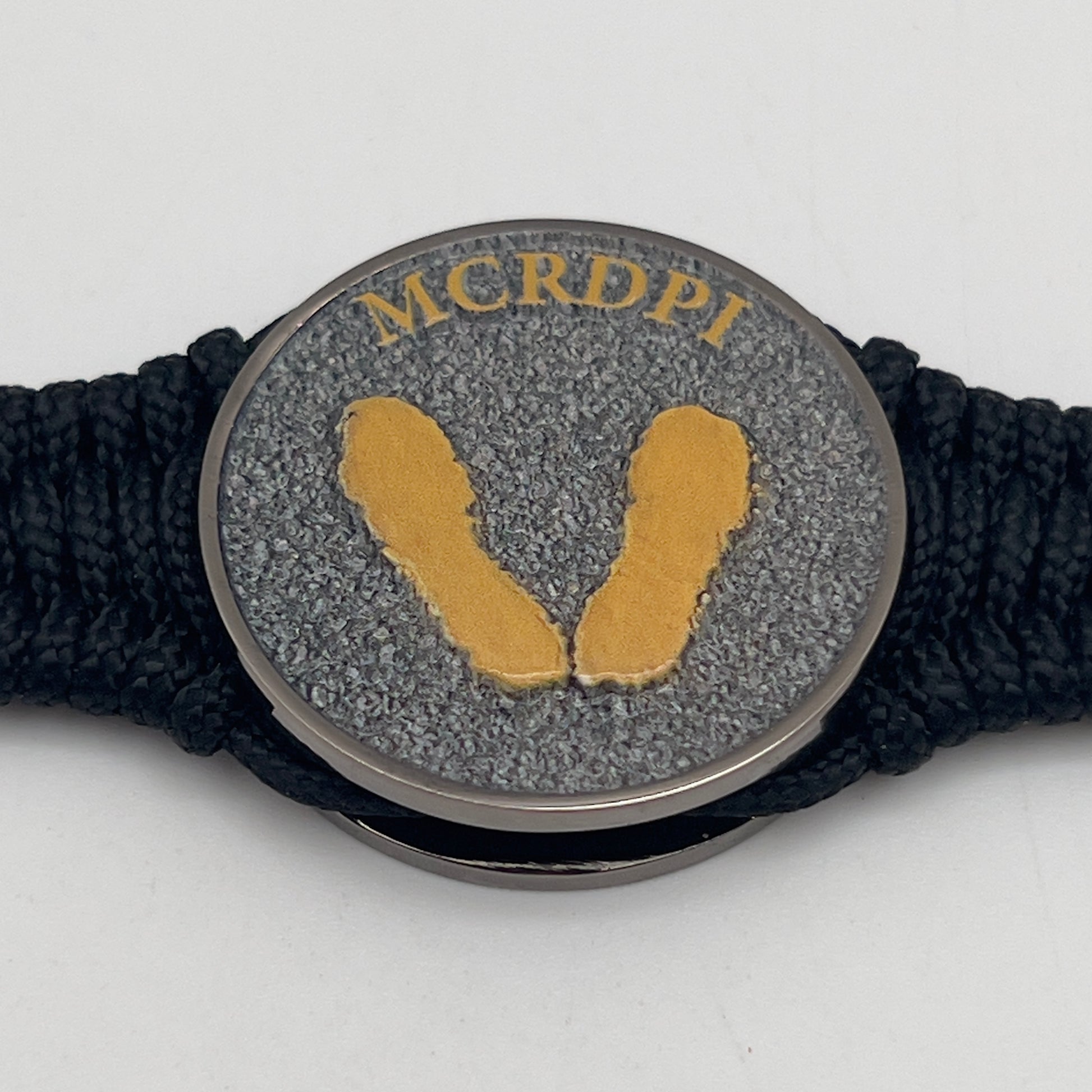Thin, narrow, flexible and comfortable braided United States Marine Corps Recruit Depot Yellow Footprints bracelet featuring a black nickel plated UV enamel painted medallion replica of an actual set of USMC footprints, a black Cobra style tactical buckle and woven with black Type-1 paracord.
