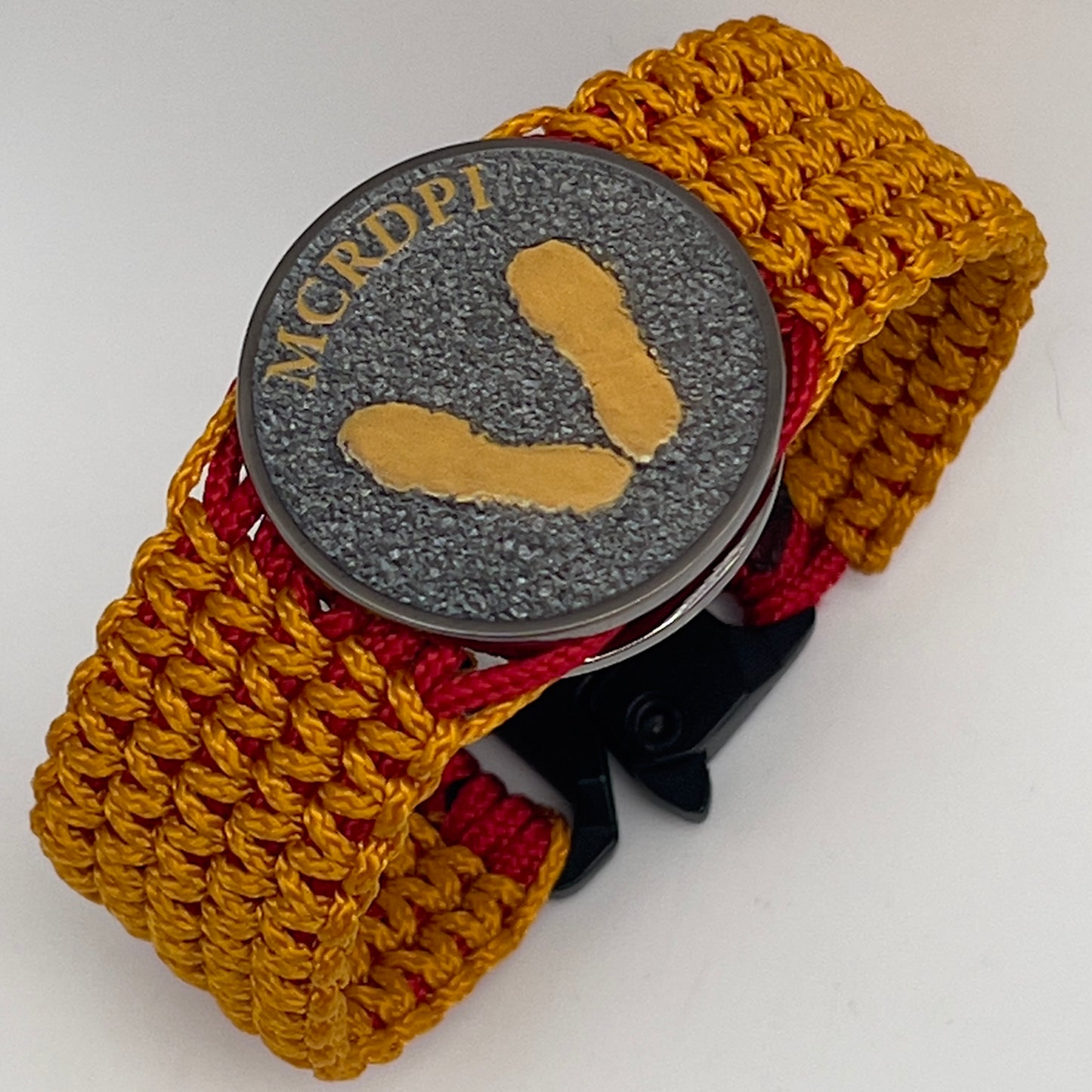 Thin, narrow, flexible and comfortable braided United States Marine Corps Recruit Depot Yellow Footprints bracelet featuring a black nickel plated UV enamel painted medallion replica of an actual set of USMC footprints, a black Cobra style tactical buckle and woven with Imperial Red type-1 paracord and Goldenrod micro cord.