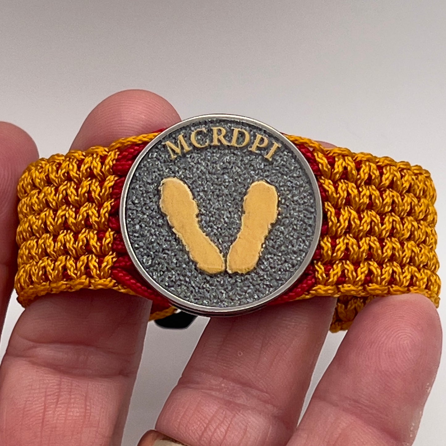 Thin, narrow, flexible and comfortable braided United States Marine Corps Recruit Depot Yellow Footprints bracelet featuring a black nickel plated UV enamel painted medallion replica of an actual set of USMC footprints, a black Cobra style tactical buckle and woven with Imperial Red type-1 paracord and Goldenrod micro cord.