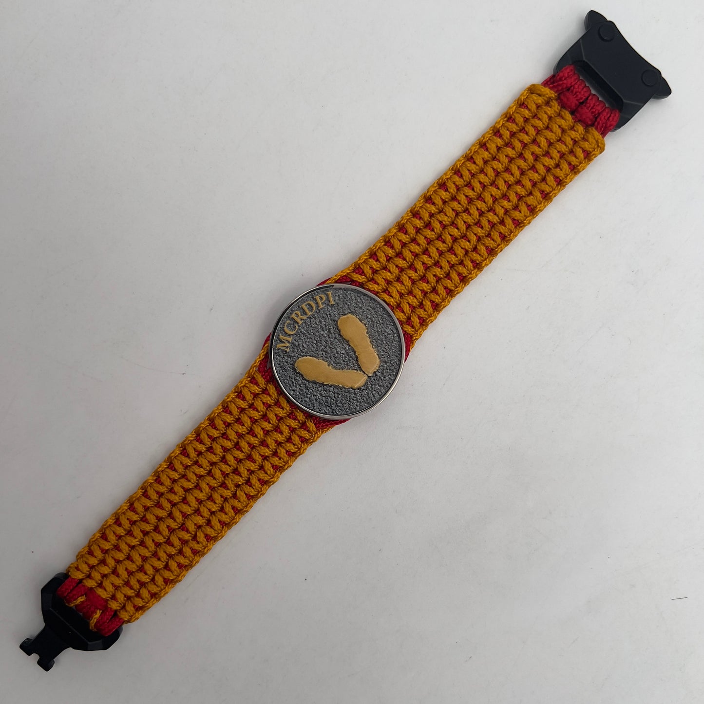 Thin, narrow, flexible and comfortable braided United States Marine Corps Recruit Depot Yellow Footprints bracelet featuring a black nickel plated UV enamel painted medallion replica of an actual set of USMC footprints, a black Cobra style tactical buckle and woven with Imperial Red type-1 paracord and Goldenrod micro cord.