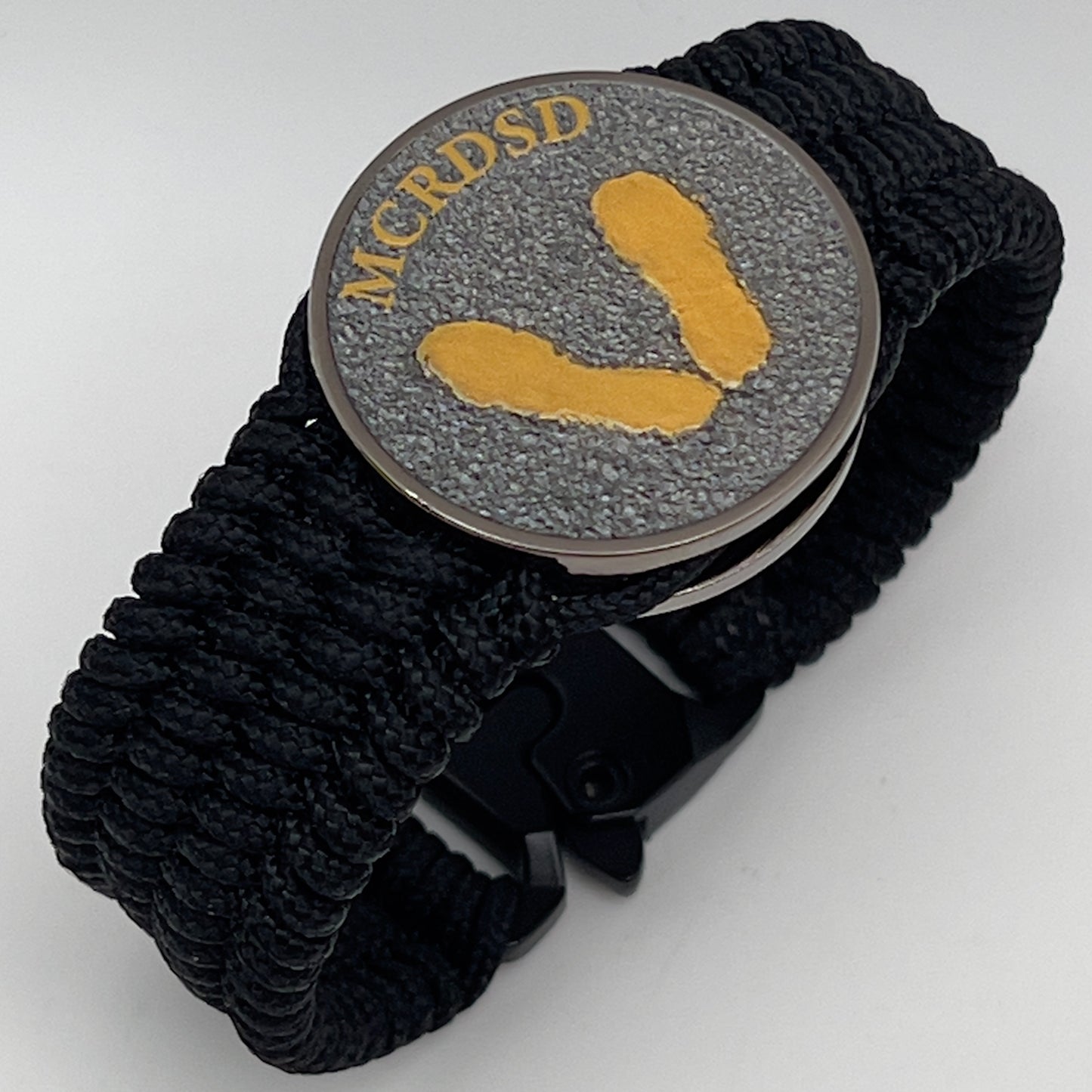 Thin, wide, flexible and comfortable braided United States Marine Corps Recruit Depot Yellow Footprints bracelet featuring a black nickel plated UV enamel painted medallion replica of an actual set of USMC footprints, a black Cobra style tactical buckle and woven with black Type-1 paracord.