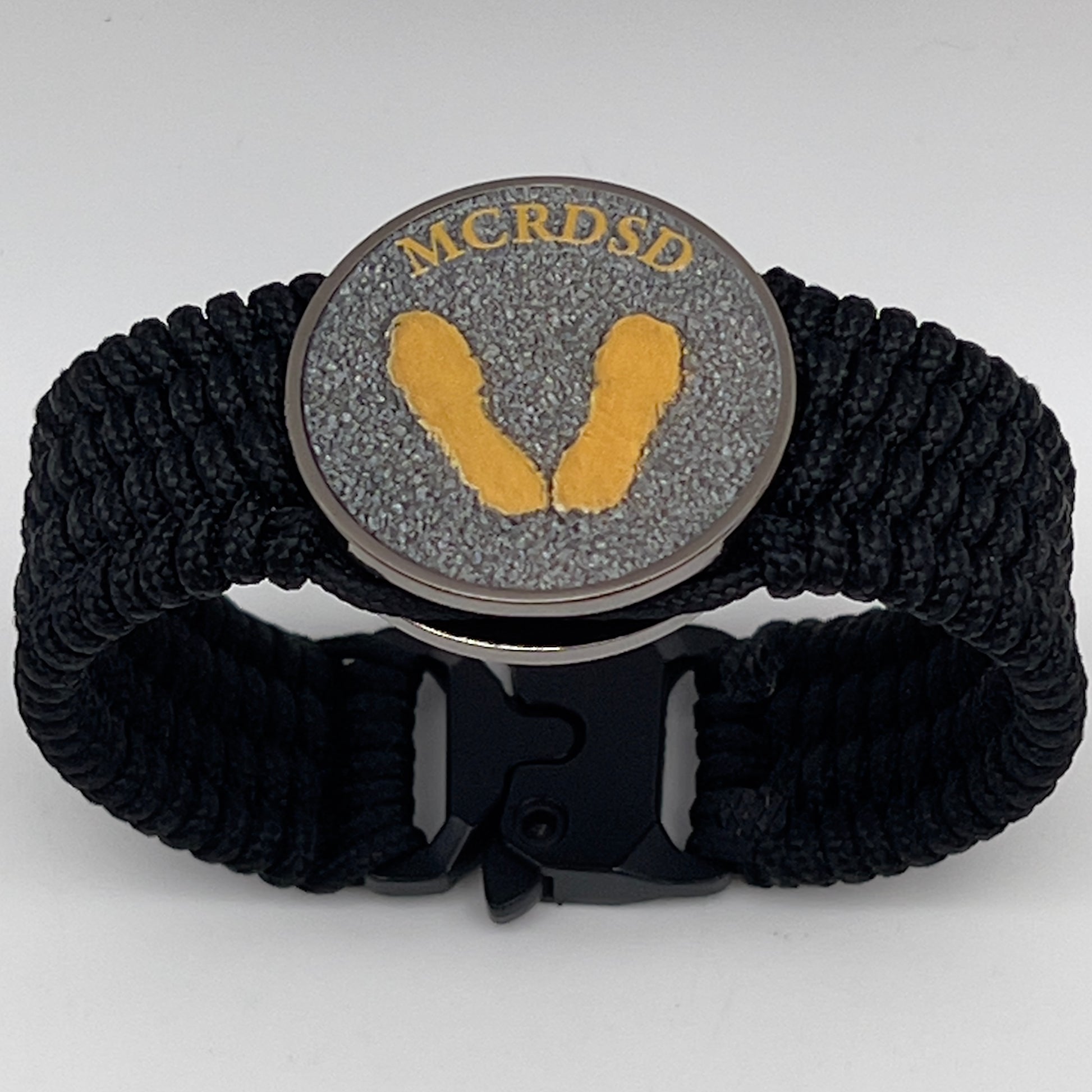 Thin, wide, flexible and comfortable braided United States Marine Corps Recruit Depot Yellow Footprints bracelet featuring a black nickel plated UV enamel painted medallion replica of an actual set of USMC footprints, a black Cobra style tactical buckle and woven with black Type-1 paracord.