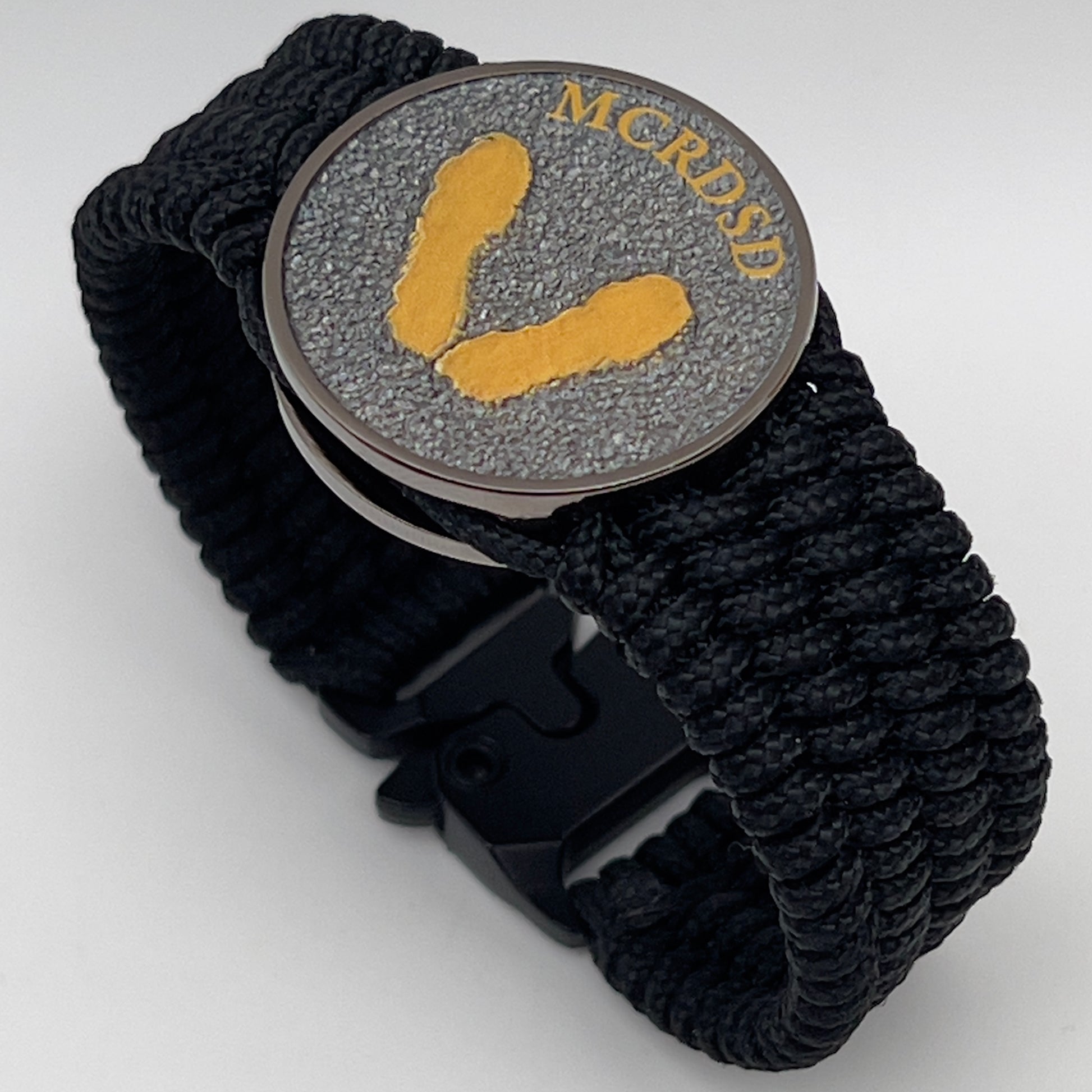 Thin, wide, flexible and comfortable braided United States Marine Corps Recruit Depot Yellow Footprints bracelet featuring a black nickel plated UV enamel painted medallion replica of an actual set of USMC footprints, a black Cobra style tactical buckle and woven with black Type-1 paracord.