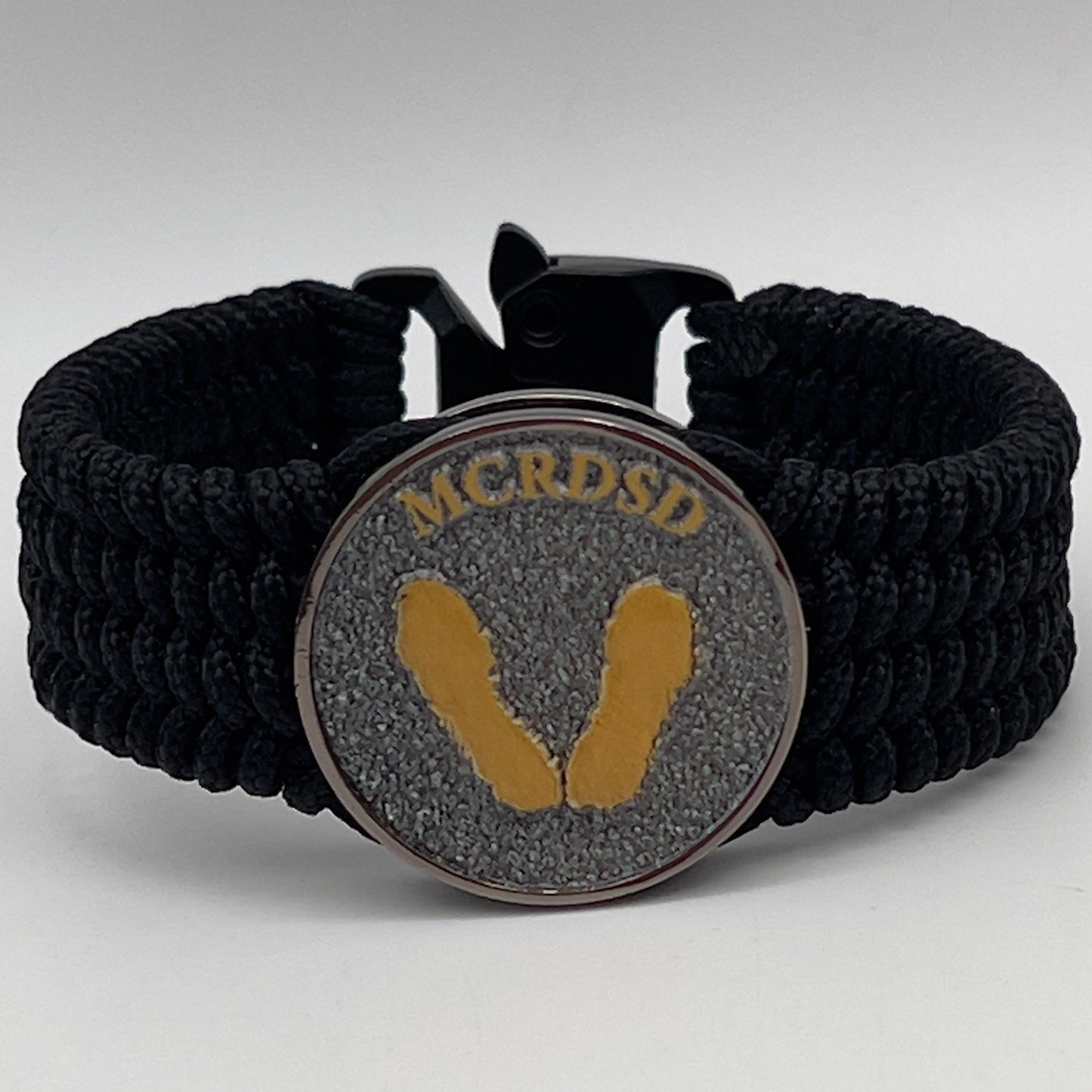 Thin, wide, flexible and comfortable braided United States Marine Corps Recruit Depot Yellow Footprints bracelet featuring a black nickel plated UV enamel painted medallion replica of an actual set of USMC footprints, a black Cobra style tactical buckle and woven with black Type-1 paracord.