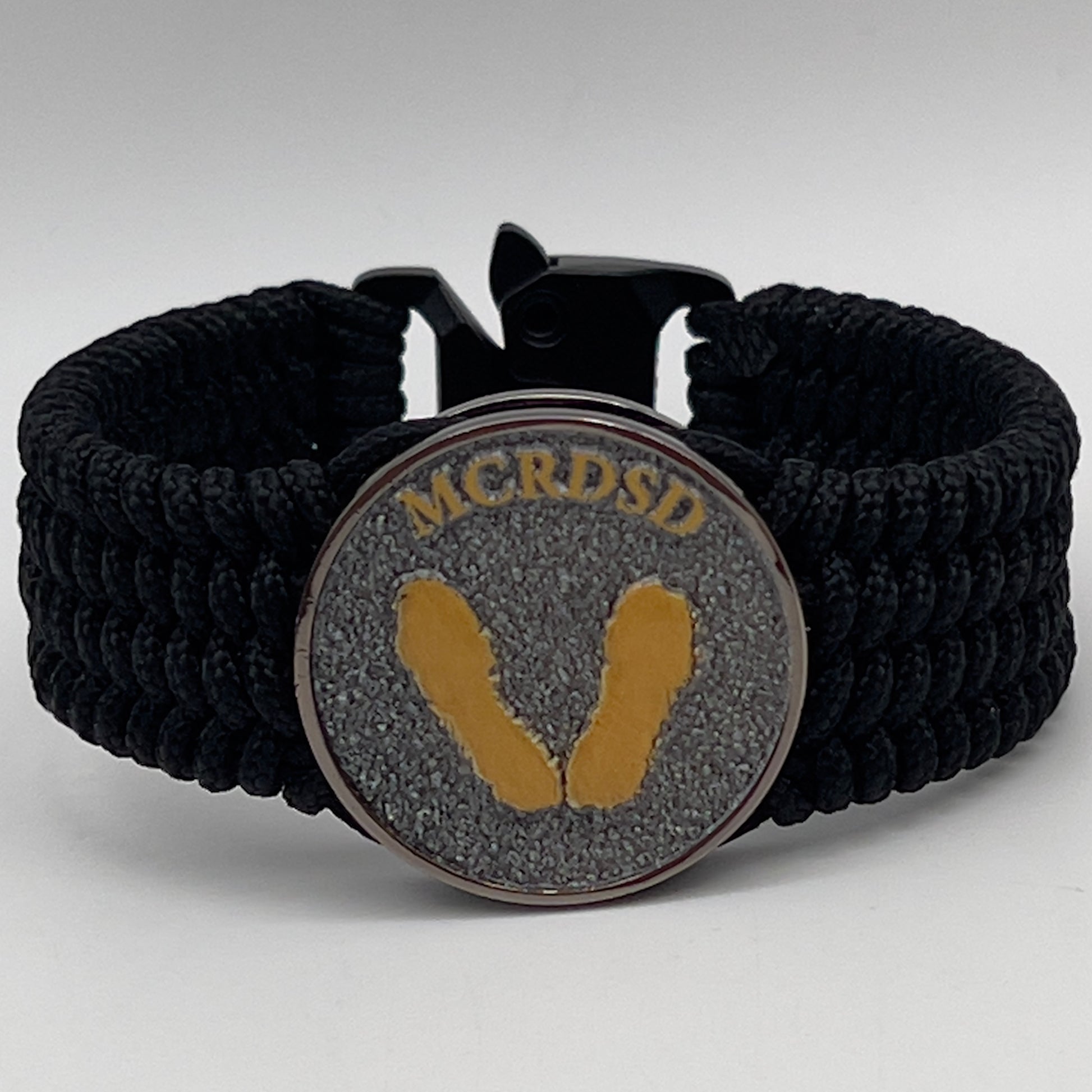 Thin, wide, flexible and comfortable braided United States Marine Corps Recruit Depot Yellow Footprints bracelet featuring a black nickel plated UV enamel painted medallion replica of an actual set of USMC footprints, a black Cobra style tactical buckle and woven with black Type-1 paracord.