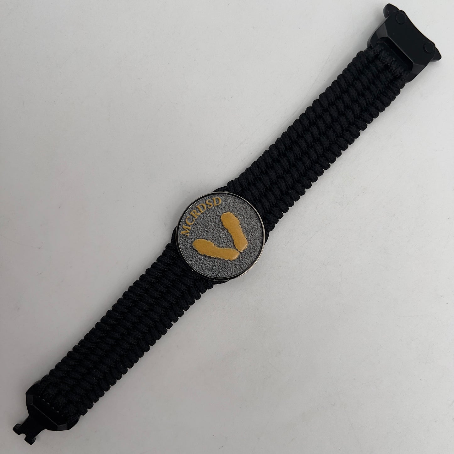 Thin, wide, flexible and comfortable braided United States Marine Corps Recruit Depot Yellow Footprints bracelet featuring a black nickel plated UV enamel painted medallion replica of an actual set of USMC footprints, a black Cobra style tactical buckle and woven with black Type-1 paracord.
