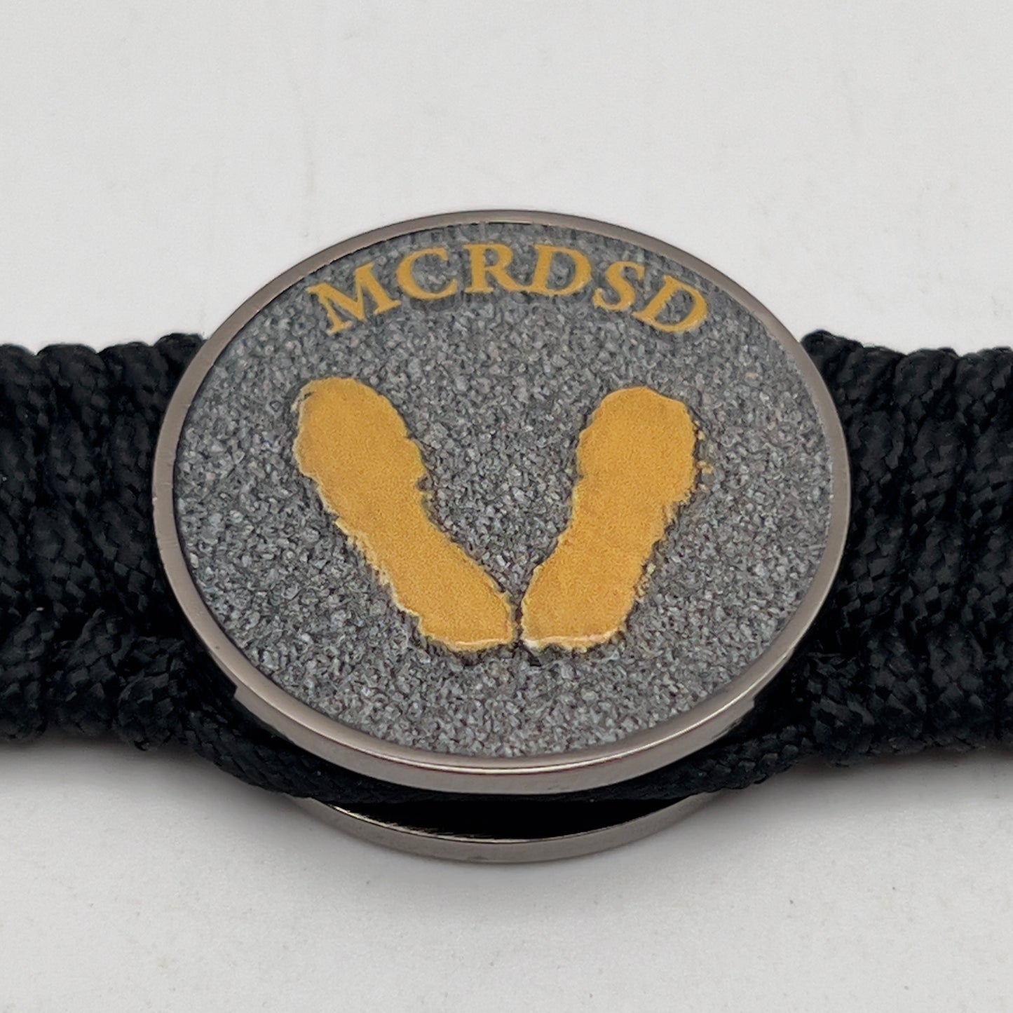 Thin, wide, flexible and comfortable braided United States Marine Corps Recruit Depot Yellow Footprints bracelet featuring a black nickel plated UV enamel painted medallion replica of an actual set of USMC footprints, a black Cobra style tactical buckle and woven with black Type-1 paracord.
