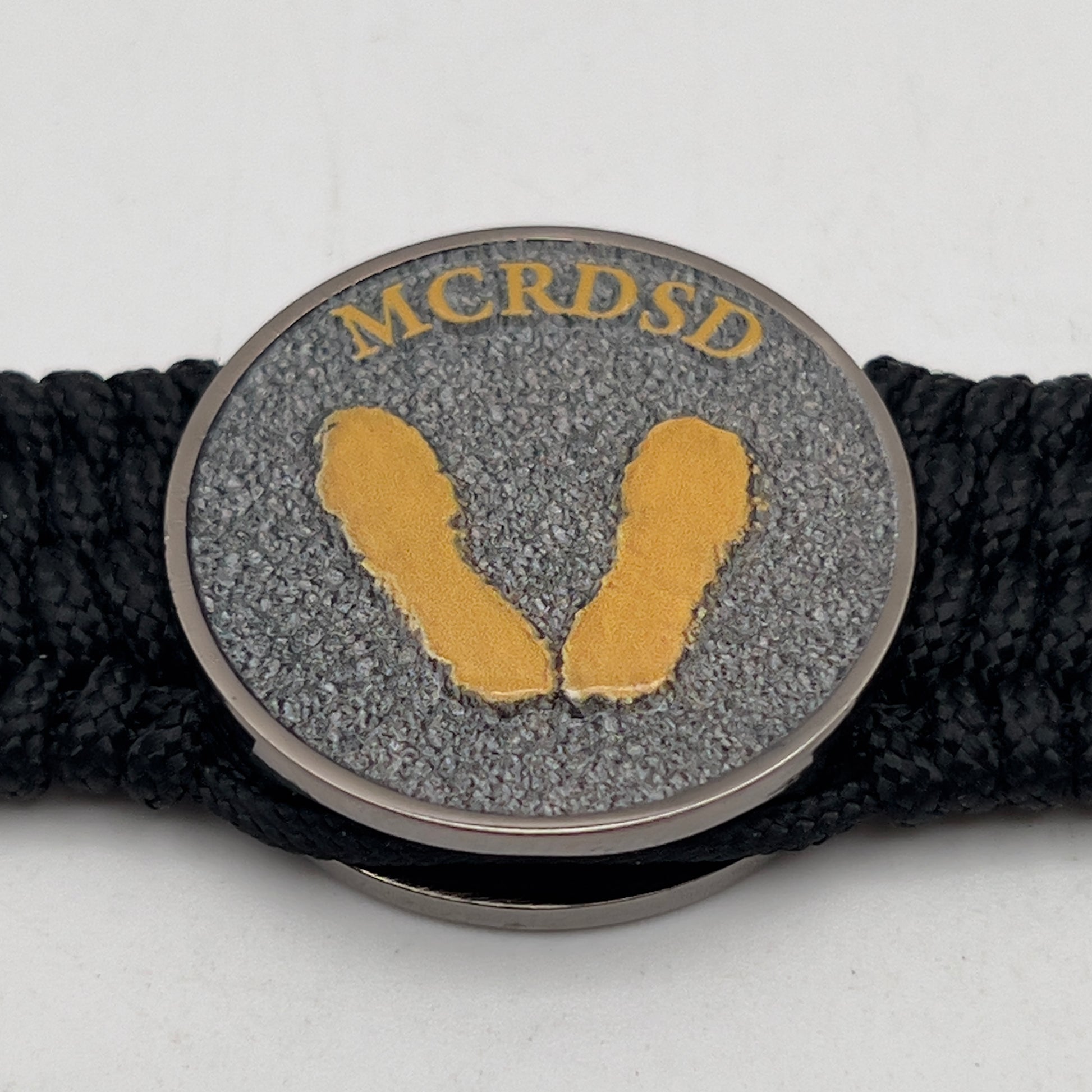 Thin, wide, flexible and comfortable braided United States Marine Corps Recruit Depot Yellow Footprints bracelet featuring a black nickel plated UV enamel painted medallion replica of an actual set of USMC footprints, a black Cobra style tactical buckle and woven with black Type-1 paracord.