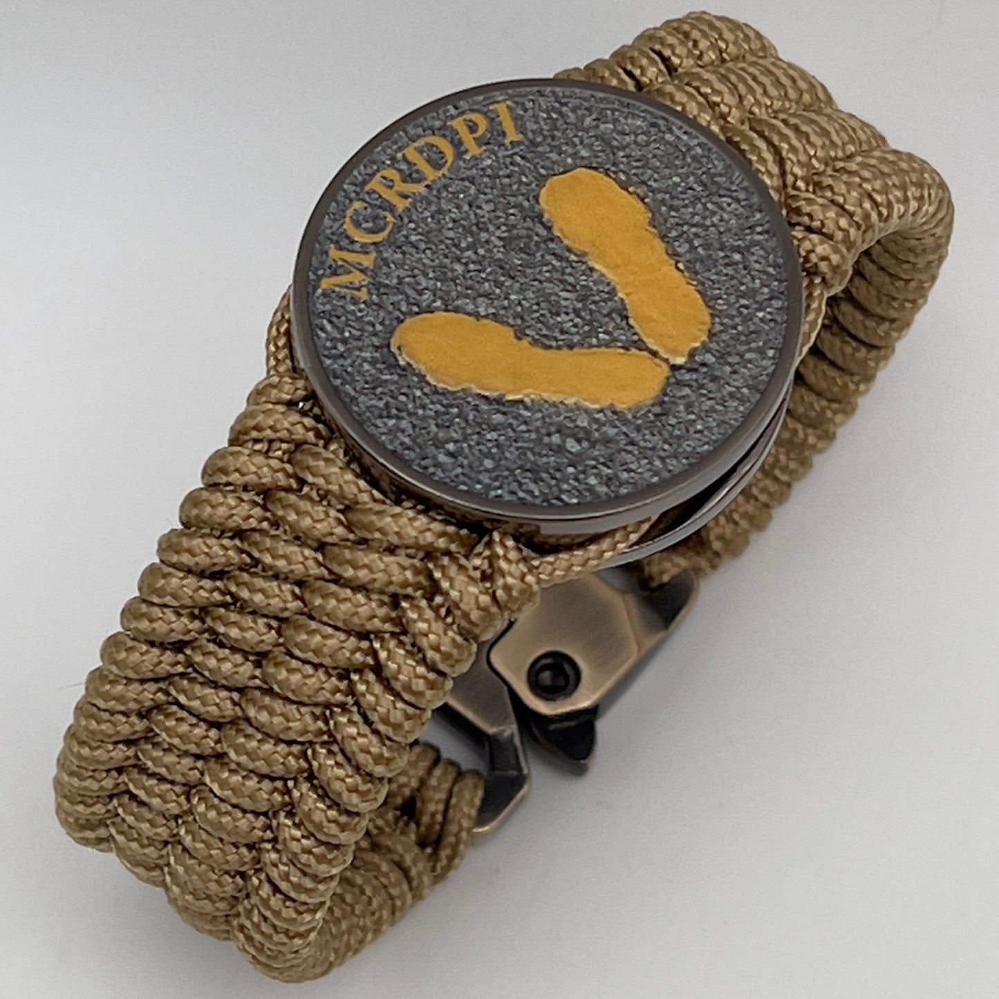 Thin, wide, flexible and comfortable braided United States Marine Corps Recruit Depot Yellow Footprints bracelet featuring a black nickel plated UV enamel painted medallion replica of an actual set of USMC footprints, a gold Cobra style tactical buckle and woven with gold Type-1 paracord.