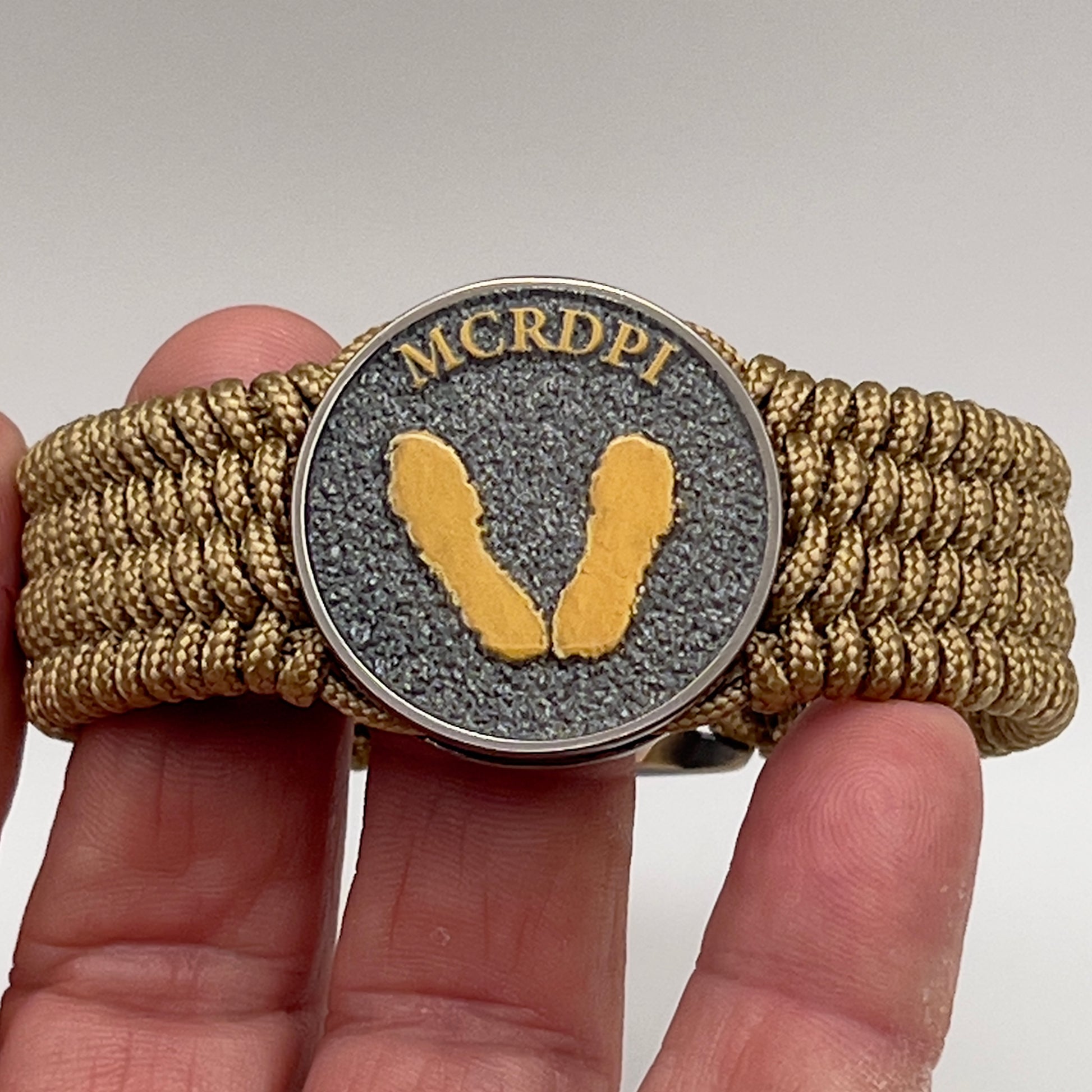 Thin, wide, flexible and comfortable braided United States Marine Corps Recruit Depot Yellow Footprints bracelet featuring a black nickel plated UV enamel painted medallion replica of an actual set of USMC footprints, a gold Cobra style tactical buckle and woven with gold Type-1 paracord.