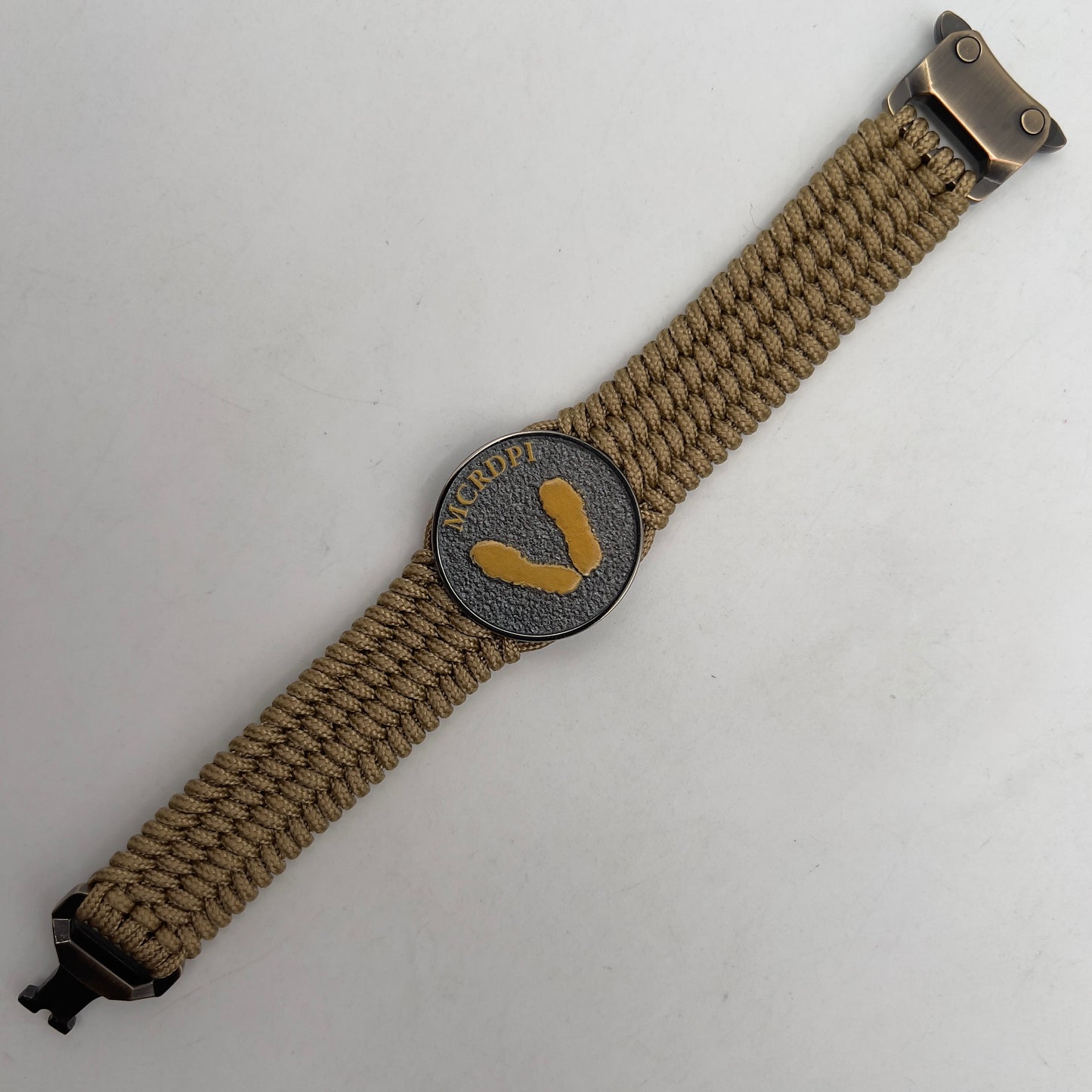 Thin, wide, flexible and comfortable braided United States Marine Corps Recruit Depot Yellow Footprints bracelet featuring a black nickel plated UV enamel painted medallion replica of an actual set of USMC footprints, a gold Cobra style tactical buckle and woven with gold Type-1 paracord.