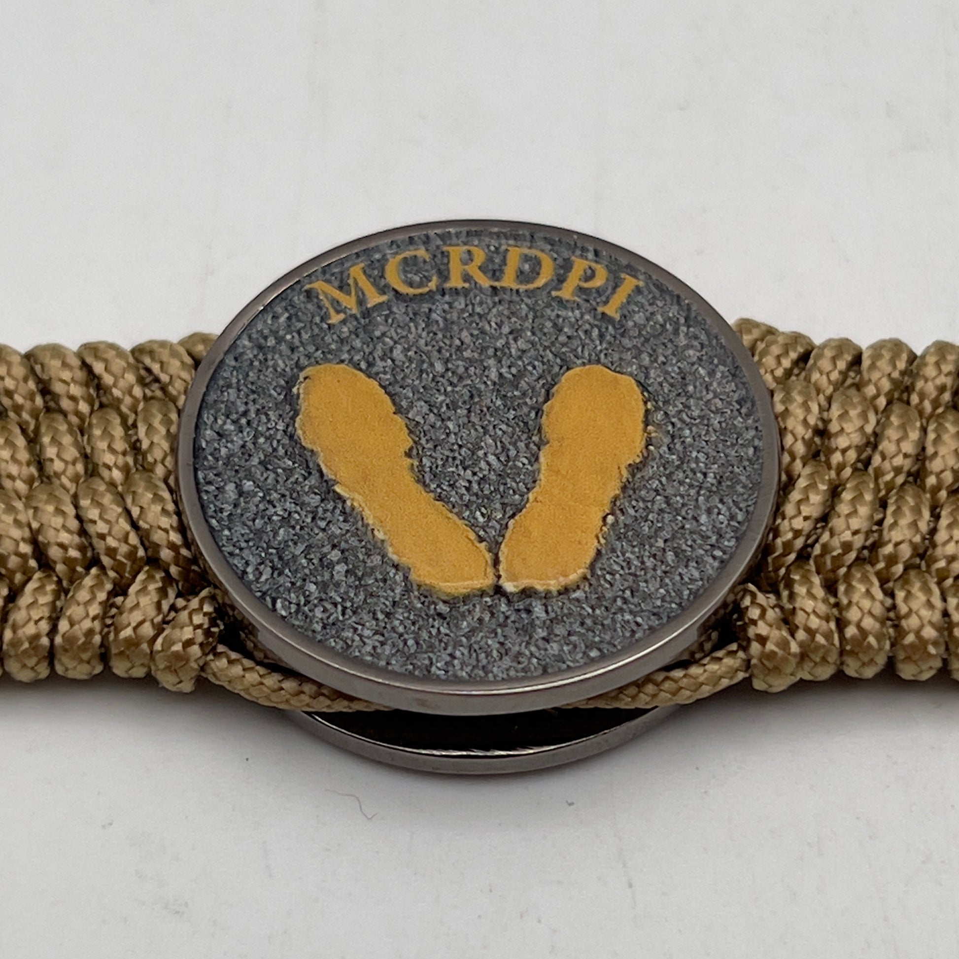 Thin, wide, flexible and comfortable braided United States Marine Corps Recruit Depot Yellow Footprints bracelet featuring a black nickel plated UV enamel painted medallion replica of an actual set of USMC footprints, a gold Cobra style tactical buckle and woven with gold Type-1 paracord.