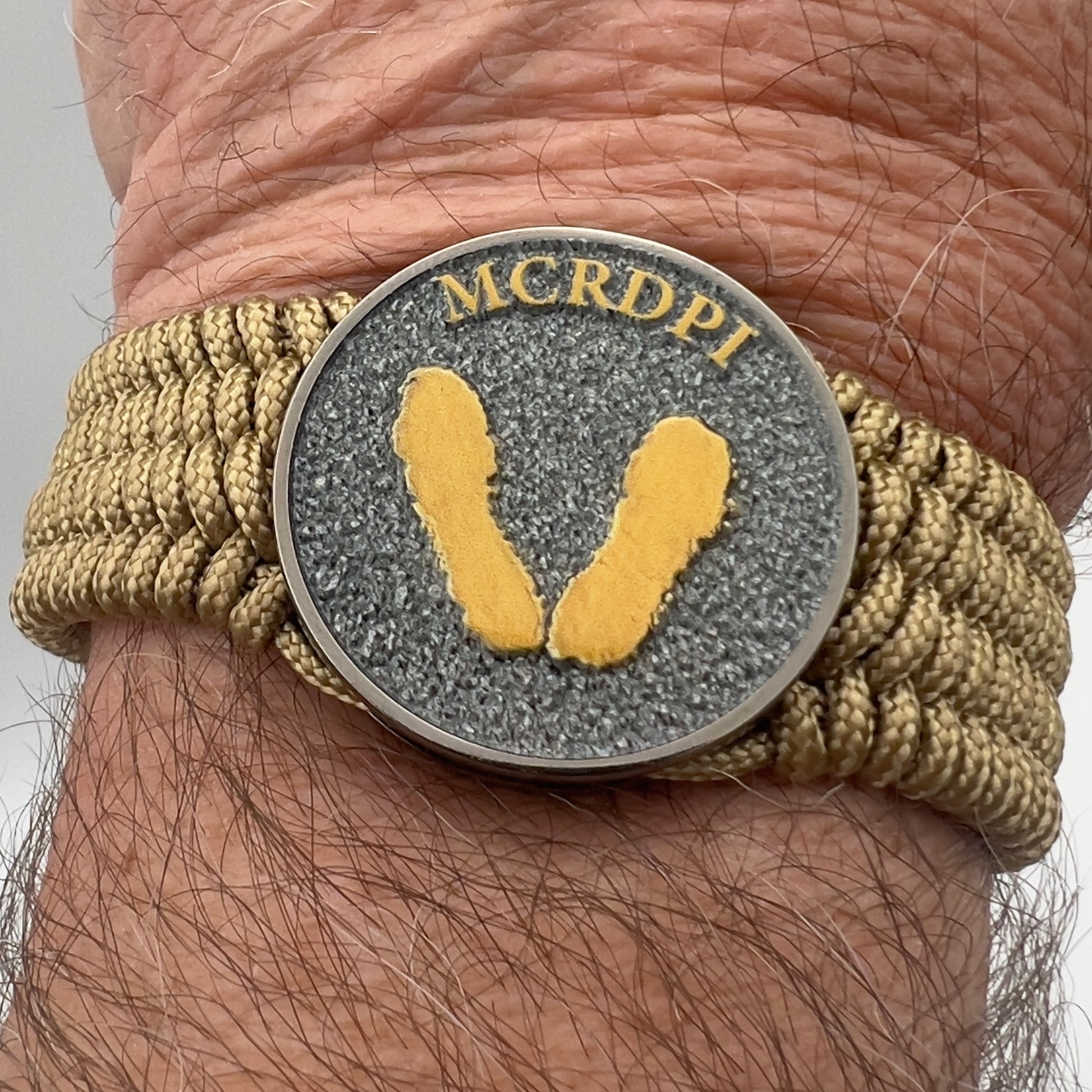 Thin, wide, flexible and comfortable braided United States Marine Corps Recruit Depot Yellow Footprints bracelet featuring a black nickel plated UV enamel painted medallion replica of an actual set of USMC footprints, a gold Cobra style tactical buckle and woven with gold Type-1 paracord.