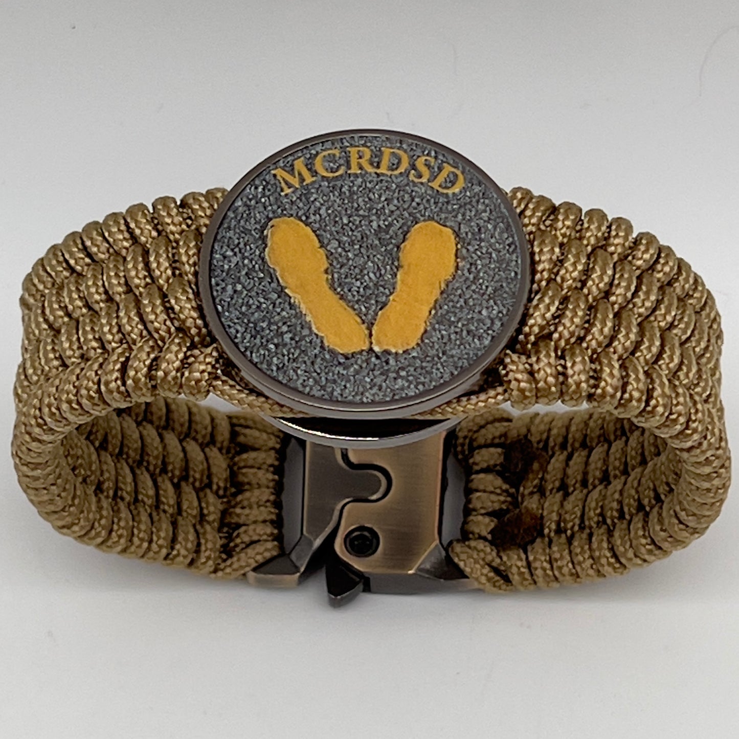 Thin, wide, flexible and comfortable braided United States Marine Corps Recruit Depot Yellow Footprints bracelet featuring a black nickel plated UV enamel painted medallion replica of an actual set of USMC footprints, a gold Cobra style tactical buckle and woven with gold Type-1 paracord.