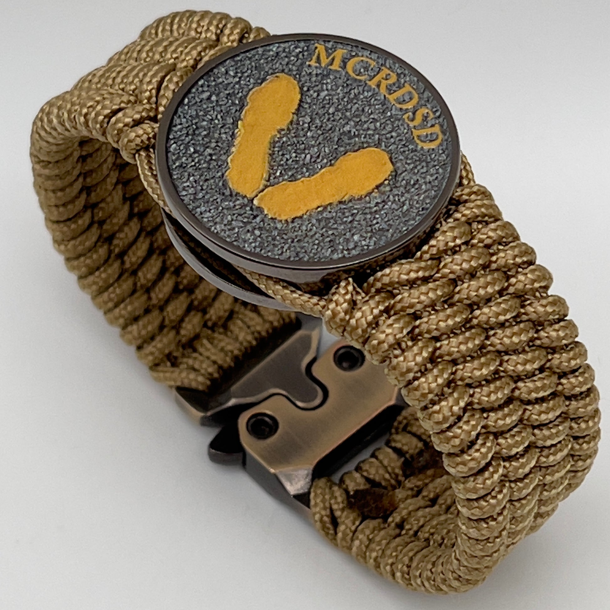 Thin, wide, flexible and comfortable braided United States Marine Corps Recruit Depot Yellow Footprints bracelet featuring a black nickel plated UV enamel painted medallion replica of an actual set of USMC footprints, a gold Cobra style tactical buckle and woven with gold Type-1 paracord.