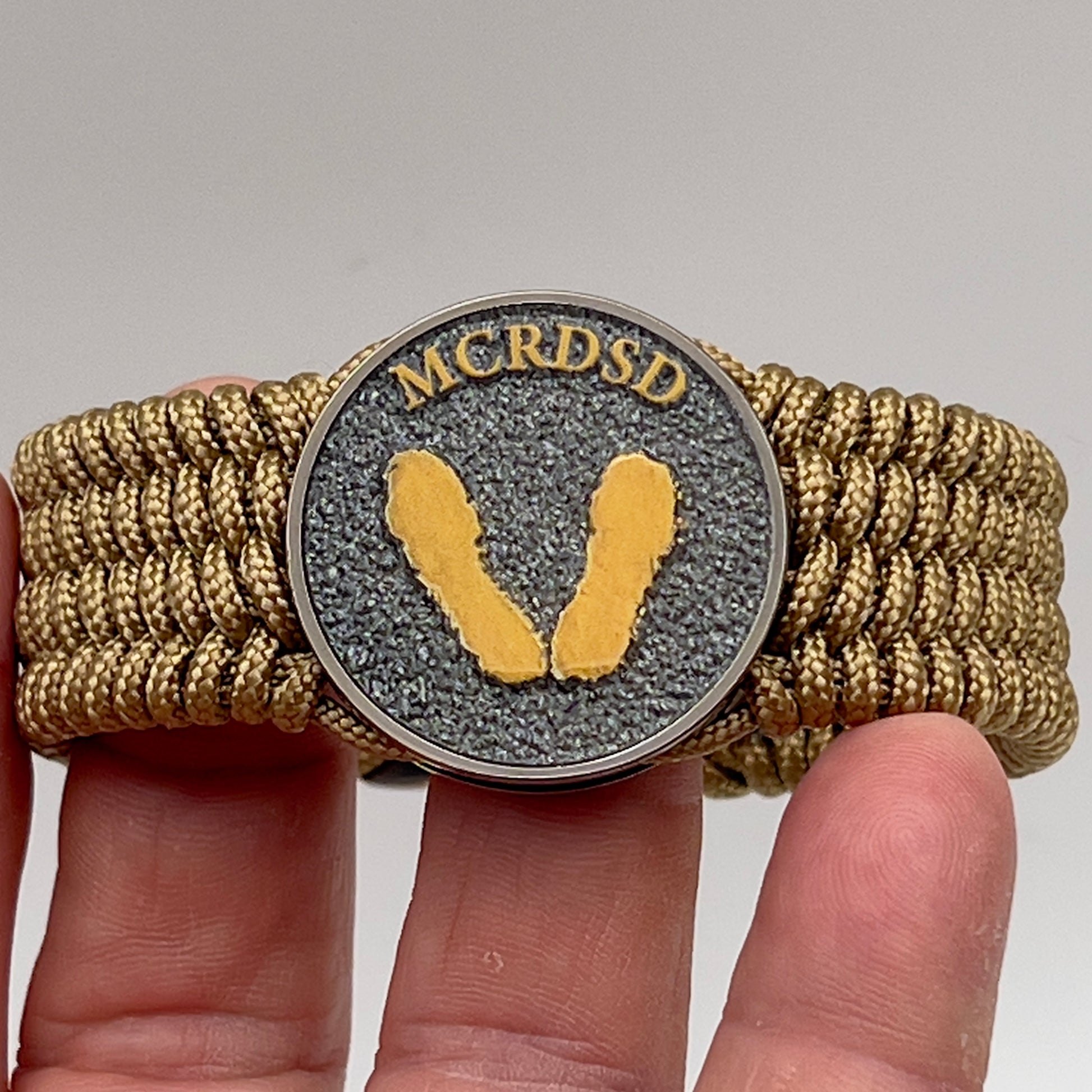 Thin, wide, flexible and comfortable braided United States Marine Corps Recruit Depot Yellow Footprints bracelet featuring a black nickel plated UV enamel painted medallion replica of an actual set of USMC footprints, a gold Cobra style tactical buckle and woven with gold Type-1 paracord.