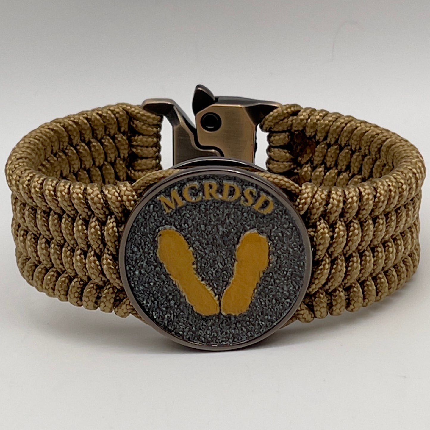Thin, wide, flexible and comfortable braided United States Marine Corps Recruit Depot Yellow Footprints bracelet featuring a black nickel plated UV enamel painted medallion replica of an actual set of USMC footprints, a gold Cobra style tactical buckle and woven with gold Type-1 paracord.
