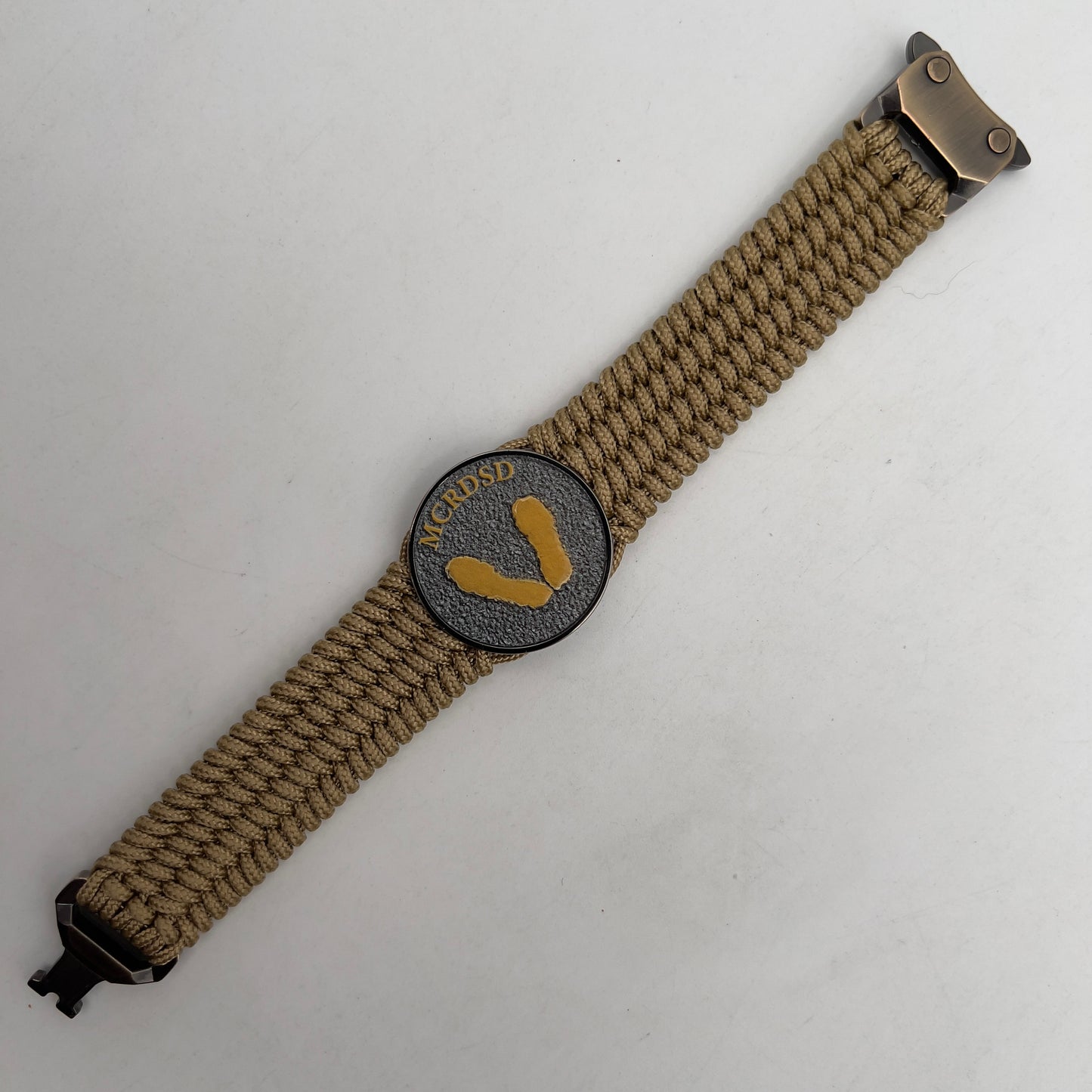 Thin, wide, flexible and comfortable braided United States Marine Corps Recruit Depot Yellow Footprints bracelet featuring a black nickel plated UV enamel painted medallion replica of an actual set of USMC footprints, a gold Cobra style tactical buckle and woven with gold Type-1 paracord.