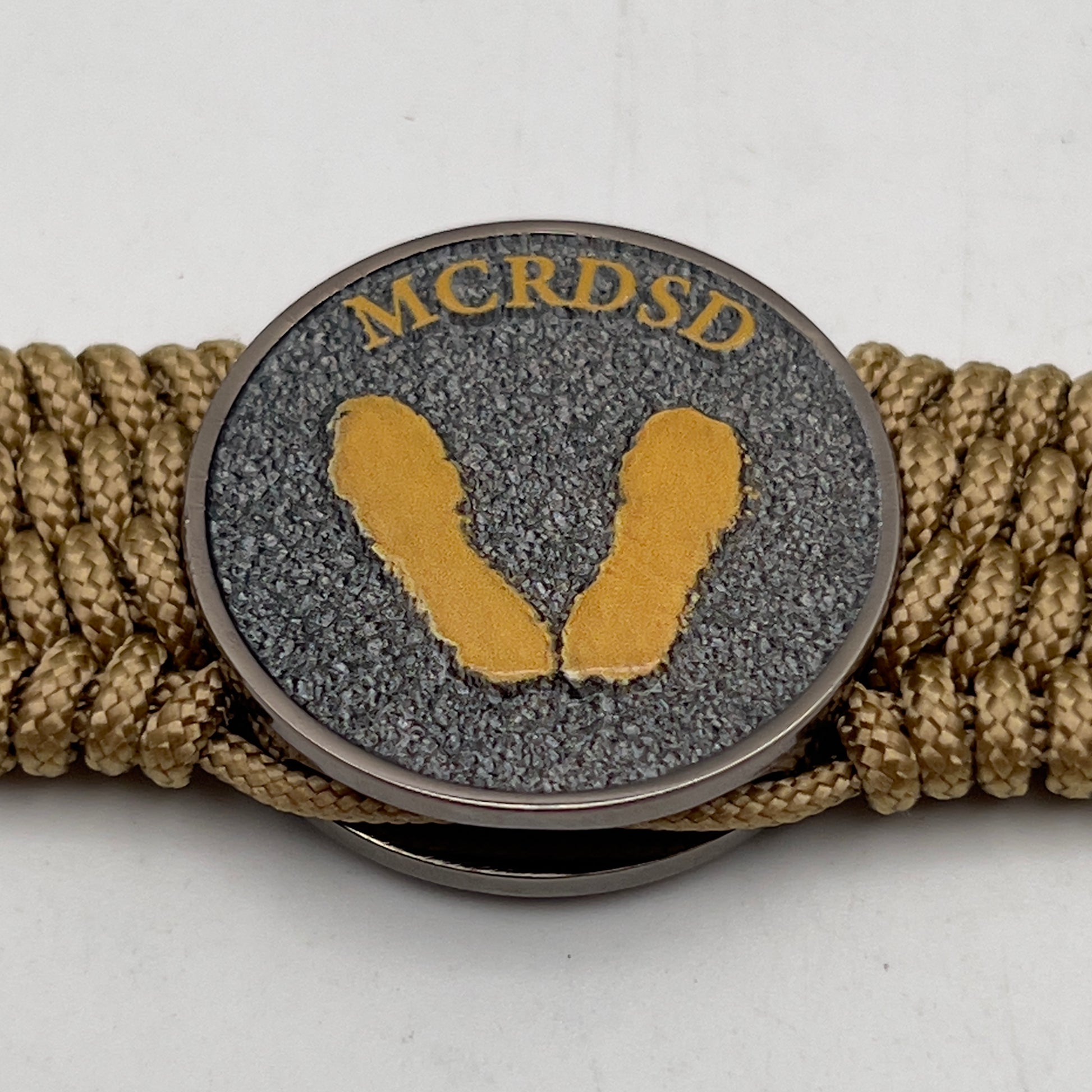 Thin, wide, flexible and comfortable braided United States Marine Corps Recruit Depot Yellow Footprints bracelet featuring a black nickel plated UV enamel painted medallion replica of an actual set of USMC footprints, a gold Cobra style tactical buckle and woven with gold Type-1 paracord.