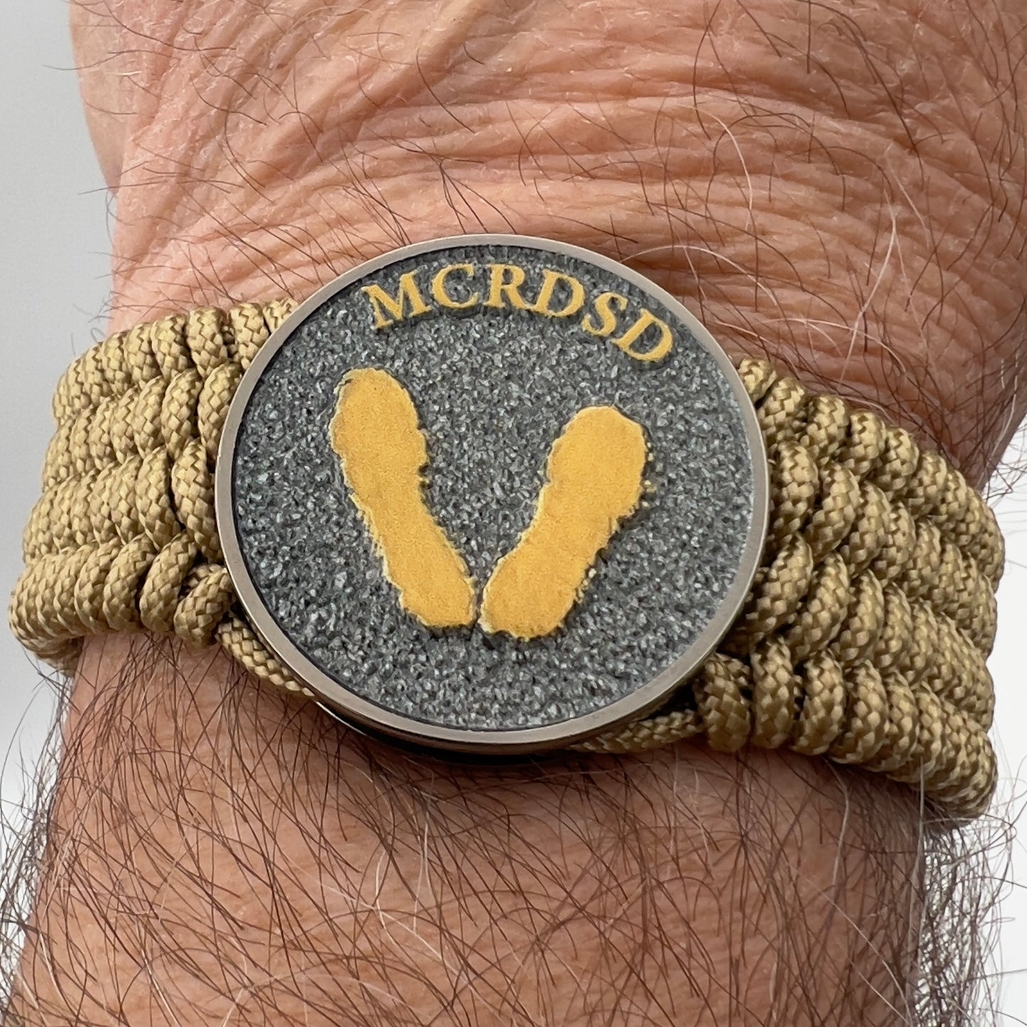 Thin, wide, flexible and comfortable braided United States Marine Corps Recruit Depot Yellow Footprints bracelet featuring a black nickel plated UV enamel painted medallion replica of an actual set of USMC footprints, a gold Cobra style tactical buckle and woven with gold Type-1 paracord.