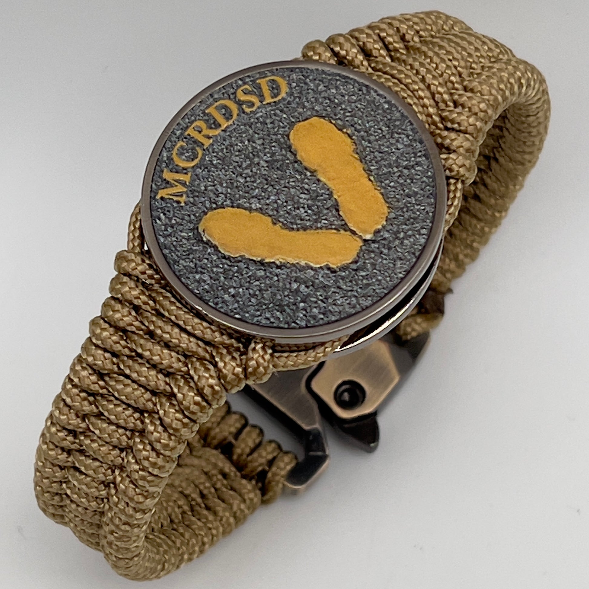 Thin, narrow, flexible and comfortable braided United States Marine Corps Recruit Depot Yellow Footprints bracelet featuring a black nickel plated UV enamel painted medallion replica of an actual set of USMC footprints, a gold Cobra style tactical buckle and woven with gold Type-1 paracord.