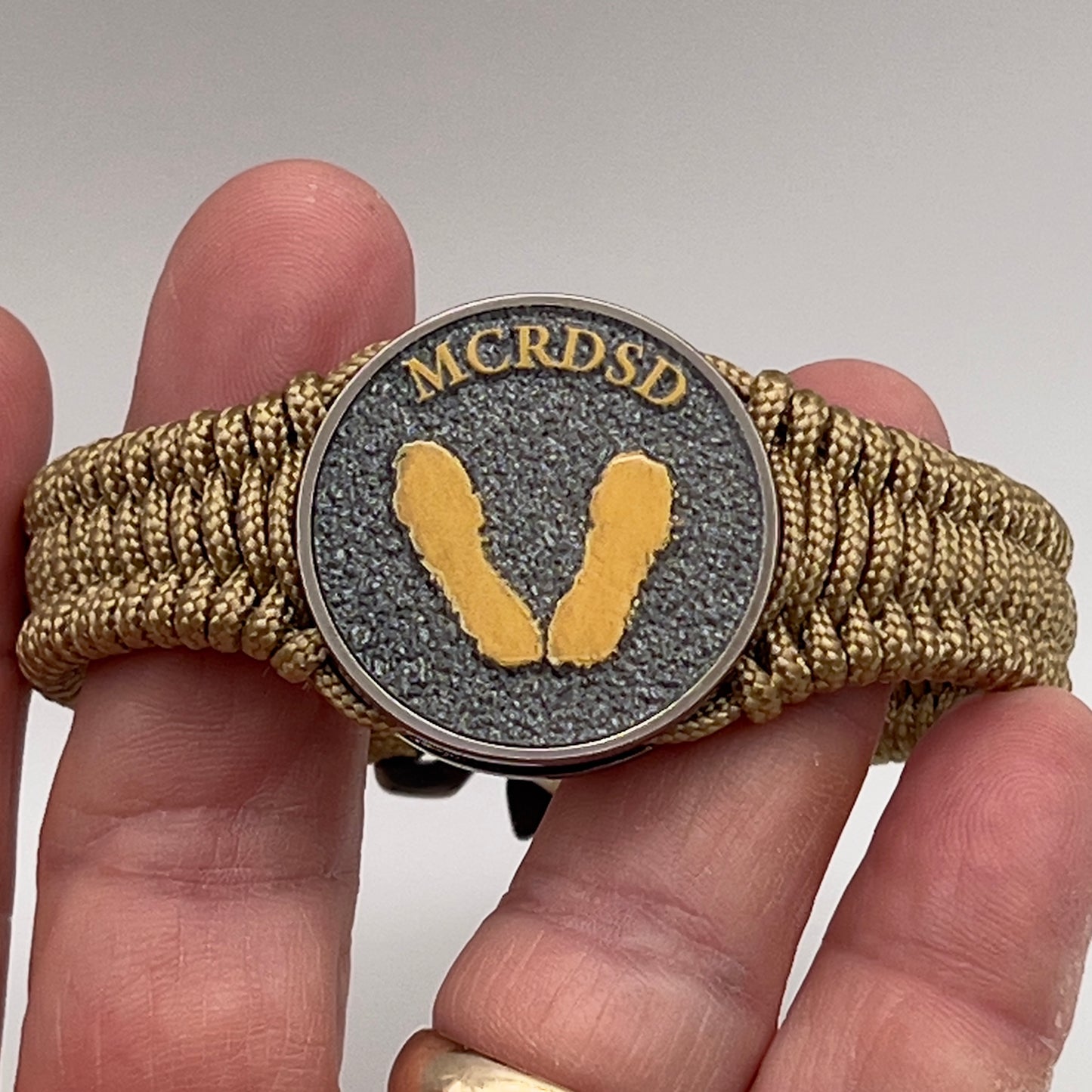 Thin, narrow, flexible and comfortable braided United States Marine Corps Recruit Depot Yellow Footprints bracelet featuring a black nickel plated UV enamel painted medallion replica of an actual set of USMC footprints, a gold Cobra style tactical buckle and woven with gold Type-1 paracord.