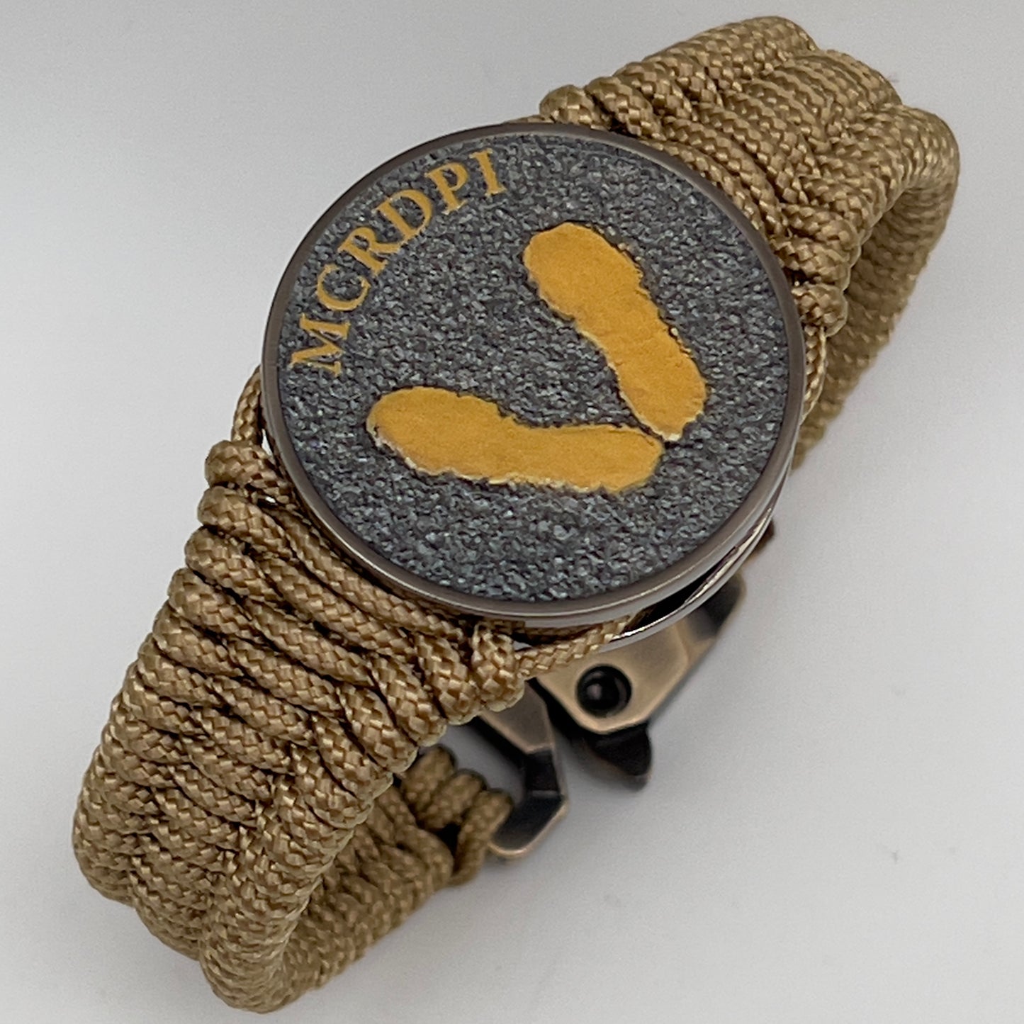 Thin, narrow, flexible and comfortable braided United States Marine Corps Recruit Depot Yellow Footprints bracelet featuring a black nickel plated UV enamel painted medallion replica of an actual set of USMC footprints, a gold Cobra style tactical buckle and woven with gold Type-1 paracord.