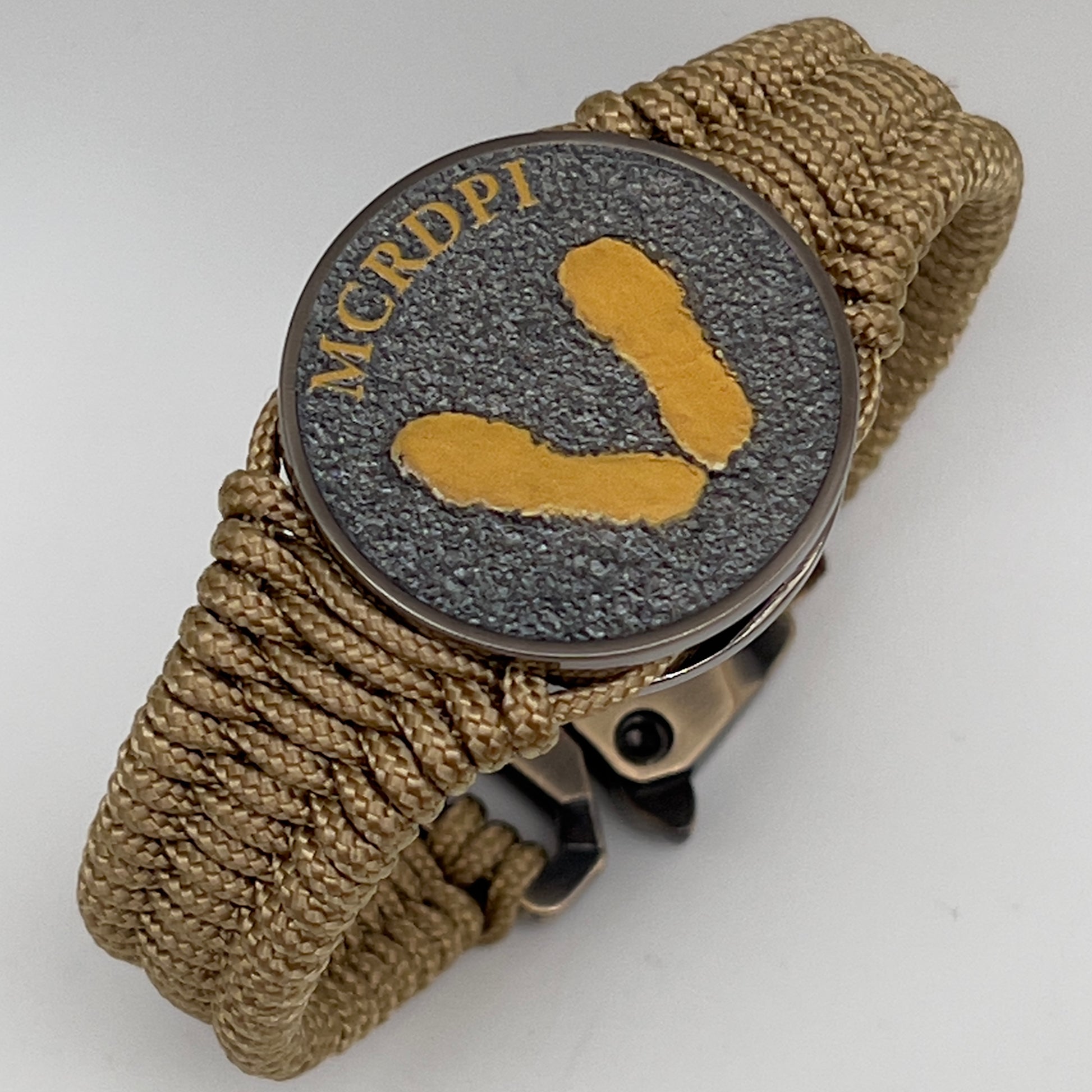 Thin, narrow, flexible and comfortable braided United States Marine Corps Recruit Depot Yellow Footprints bracelet featuring a black nickel plated UV enamel painted medallion replica of an actual set of USMC footprints, a gold Cobra style tactical buckle and woven with gold Type-1 paracord.