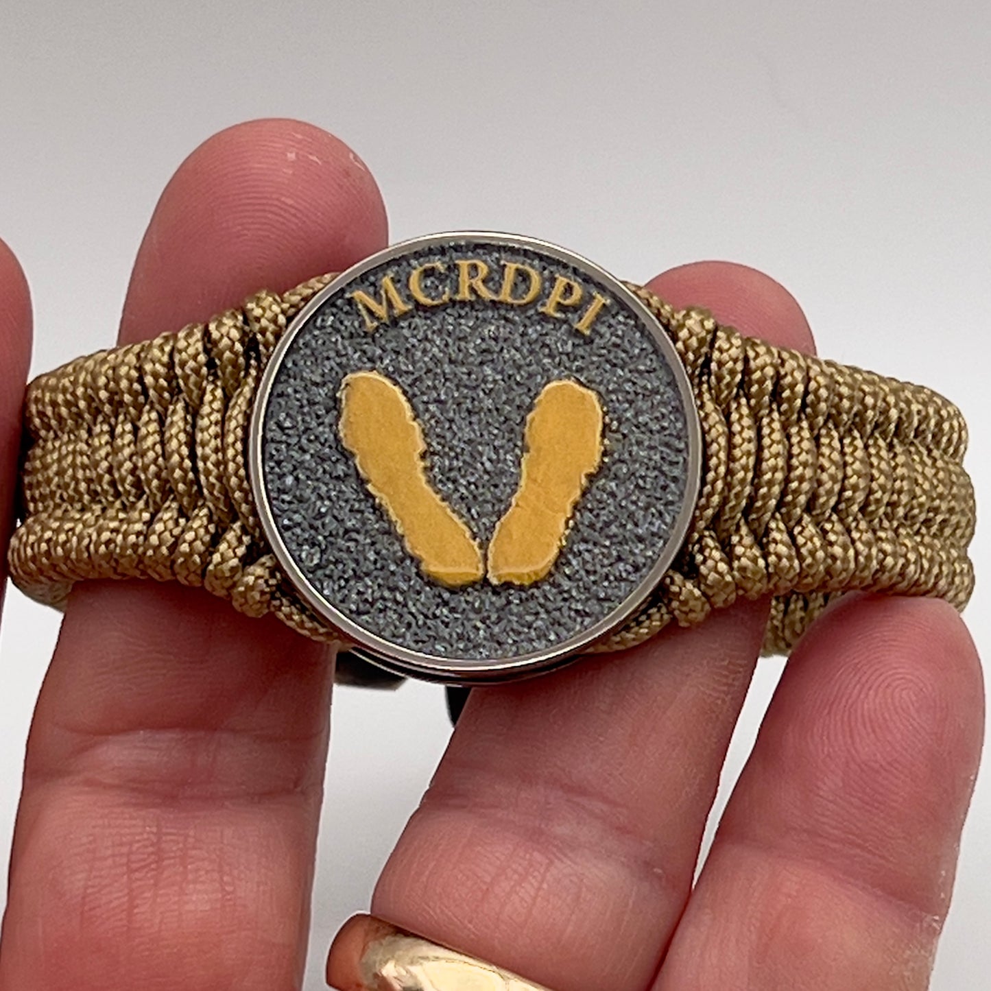 Thin, narrow, flexible and comfortable braided United States Marine Corps Recruit Depot Yellow Footprints bracelet featuring a black nickel plated UV enamel painted medallion replica of an actual set of USMC footprints, a gold Cobra style tactical buckle and woven with gold Type-1 paracord.