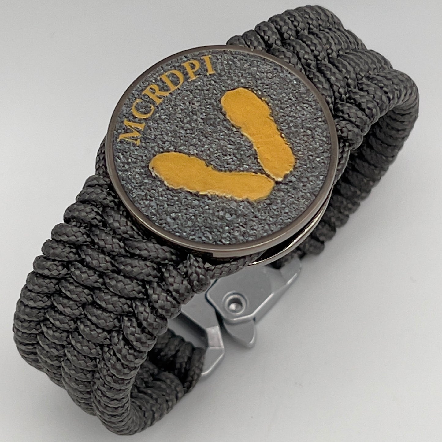 Thin, wide, flexible and comfortable braided United States Marine Corps Recruit Depot Yellow Footprints bracelet featuring a black nickel plated UV enamel painted medallion replica of an actual set of USMC footprints, a silver Cobra style tactical buckle and woven with Charcoal Gray Type-1 paracord.
