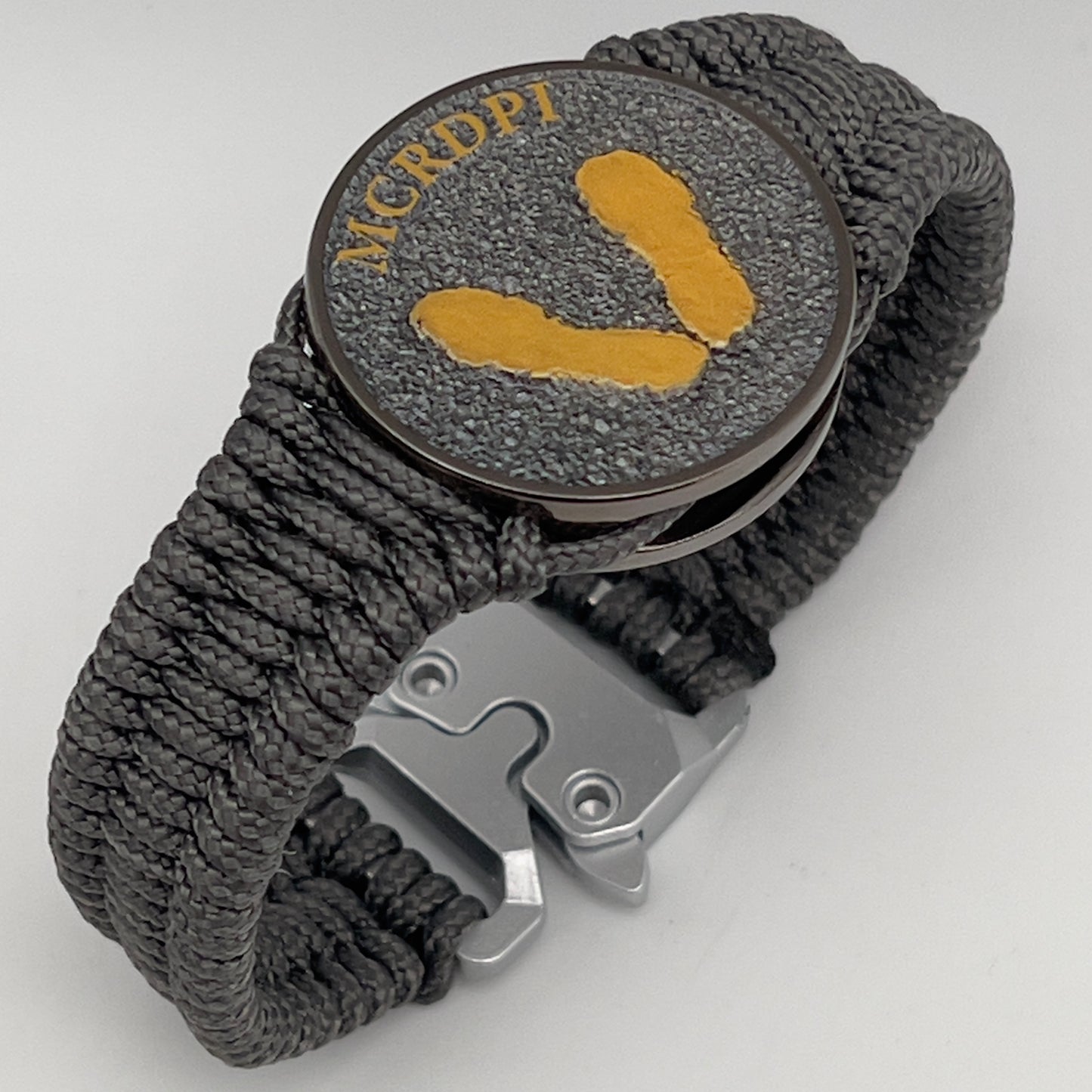 Thin, narrow, flexible and comfortable braided United States Marine Corps Recruit Depot Yellow Footprints bracelet featuring a black nickel plated UV enamel painted medallion replica of an actual set of USMC footprints, a silver Cobra style tactical buckle and woven with Charcoal Gray Type-1 paracord.