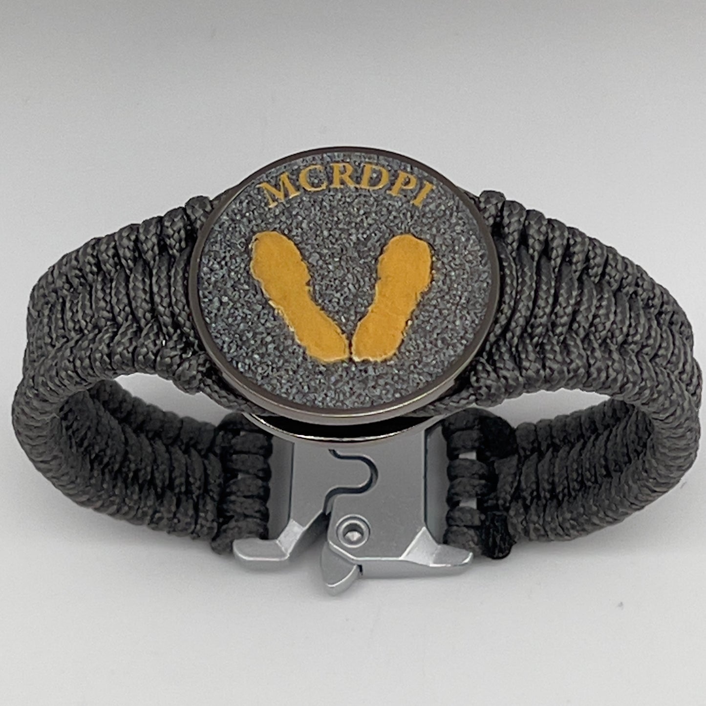 Thin, narrow, flexible and comfortable braided United States Marine Corps Recruit Depot Yellow Footprints bracelet featuring a black nickel plated UV enamel painted medallion replica of an actual set of USMC footprints, a silver Cobra style tactical buckle and woven with Charcoal Gray Type-1 paracord.