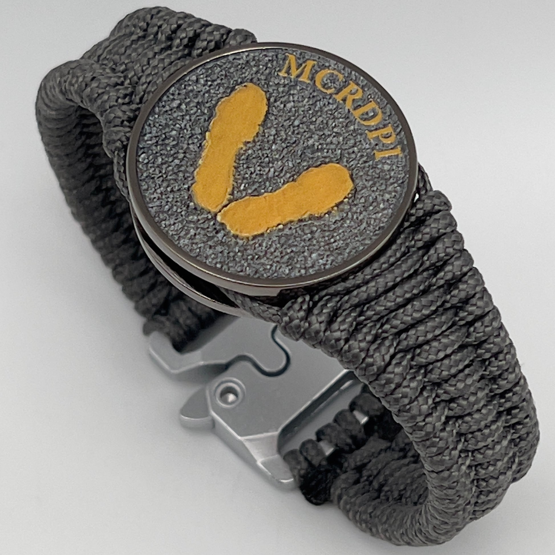 Thin, narrow, flexible and comfortable braided United States Marine Corps Recruit Depot Yellow Footprints bracelet featuring a black nickel plated UV enamel painted medallion replica of an actual set of USMC footprints, a silver Cobra style tactical buckle and woven with Charcoal Gray Type-1 paracord.