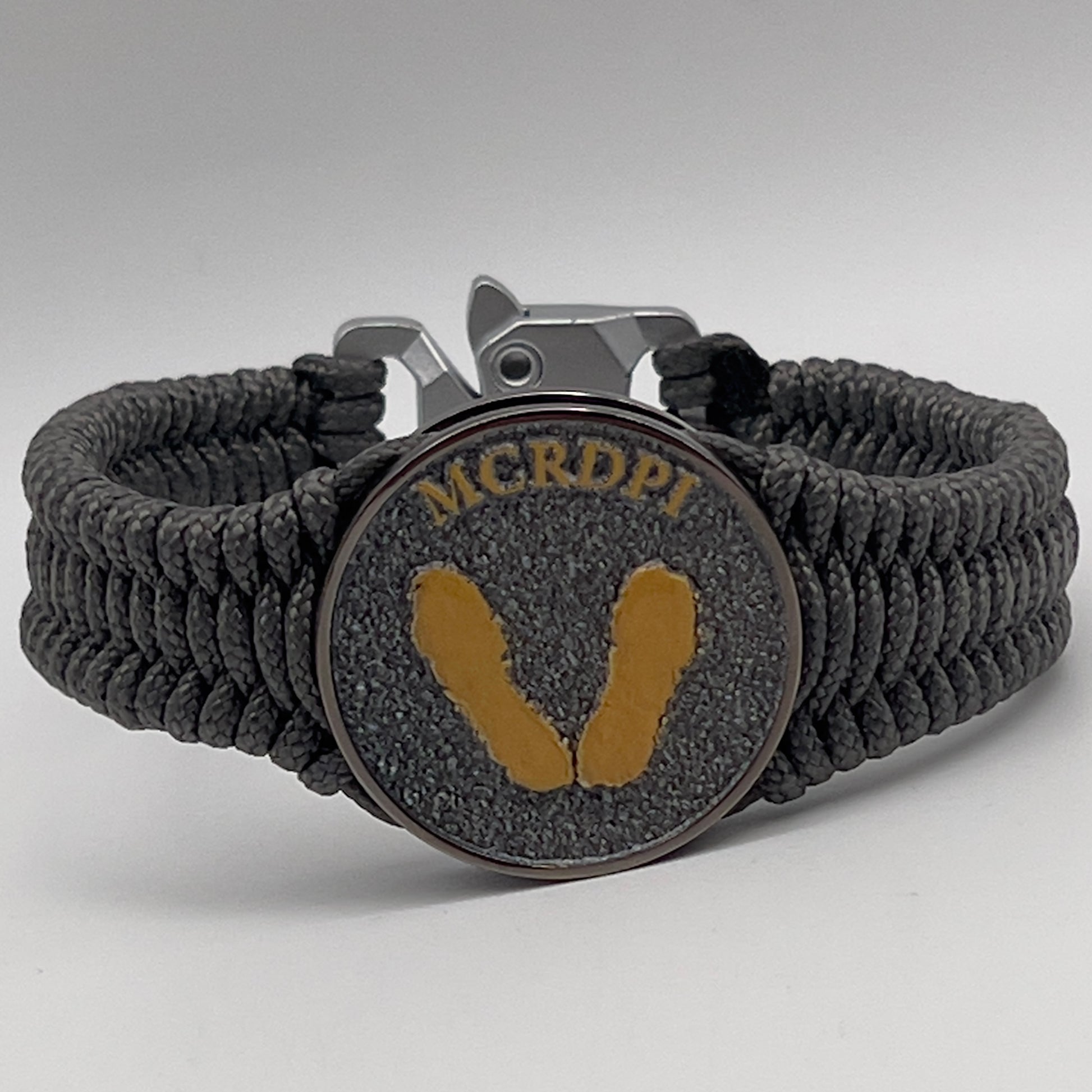 Thin, narrow, flexible and comfortable braided United States Marine Corps Recruit Depot Yellow Footprints bracelet featuring a black nickel plated UV enamel painted medallion replica of an actual set of USMC footprints, a silver Cobra style tactical buckle and woven with Charcoal Gray Type-1 paracord.