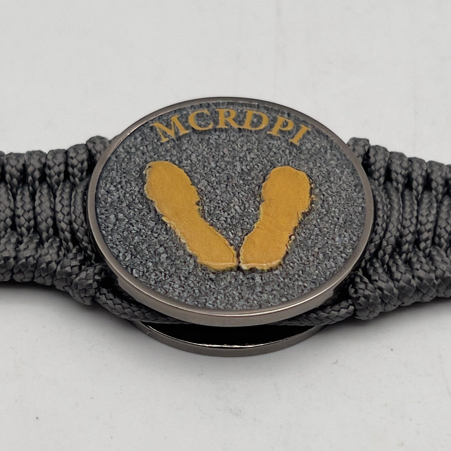Thin, narrow, flexible and comfortable braided United States Marine Corps Recruit Depot Yellow Footprints bracelet featuring a black nickel plated UV enamel painted medallion replica of an actual set of USMC footprints, a silver Cobra style tactical buckle and woven with Charcoal Gray Type-1 paracord.