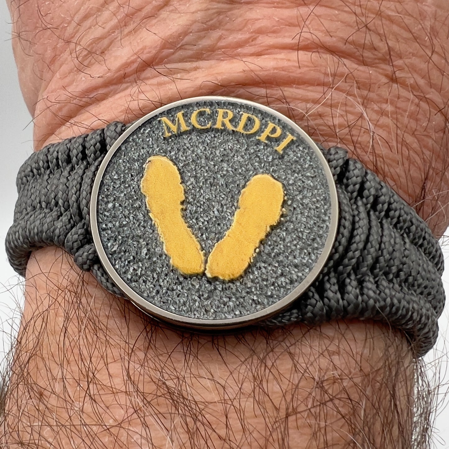 Thin, narrow, flexible and comfortable braided United States Marine Corps Recruit Depot Yellow Footprints bracelet featuring a black nickel plated UV enamel painted medallion replica of an actual set of USMC footprints, a silver Cobra style tactical buckle and woven with Charcoal Gray Type-1 paracord.