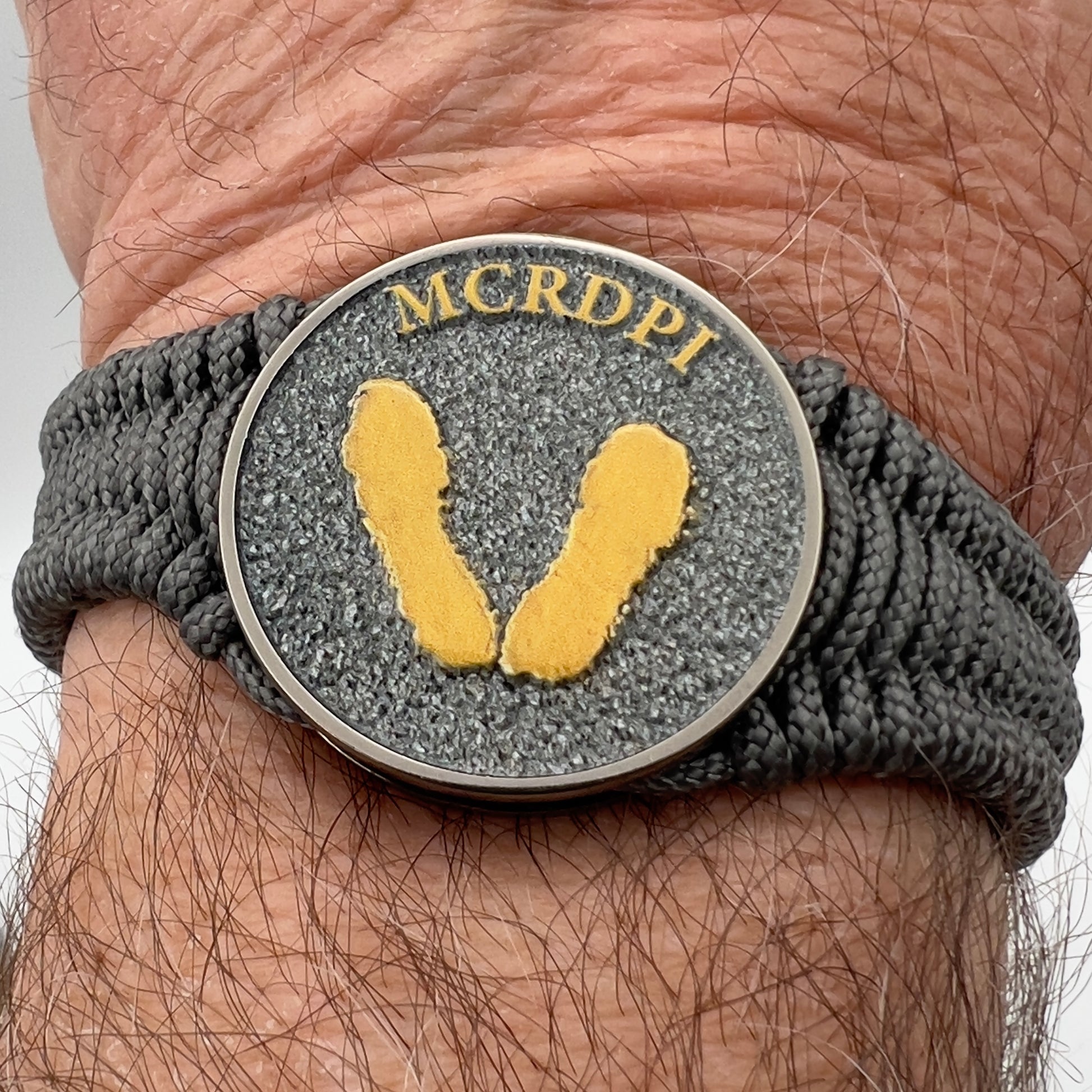 Thin, narrow, flexible and comfortable braided United States Marine Corps Recruit Depot Yellow Footprints bracelet featuring a black nickel plated UV enamel painted medallion replica of an actual set of USMC footprints, a silver Cobra style tactical buckle and woven with Charcoal Gray Type-1 paracord.