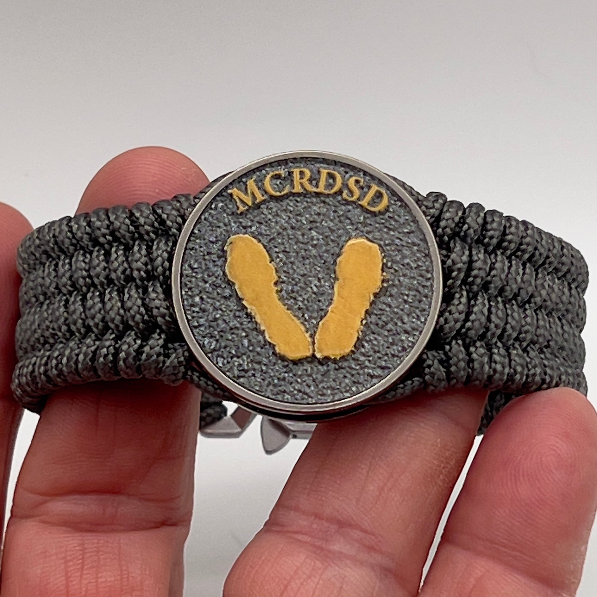 Thin, wide, flexible and comfortable braided United States Marine Corps Recruit Depot Yellow Footprints bracelet featuring a black nickel plated UV enamel painted medallion replica of an actual set of USMC footprints, a silver Cobra style tactical buckle and woven with Charcoal Gray Type-1 paracord.