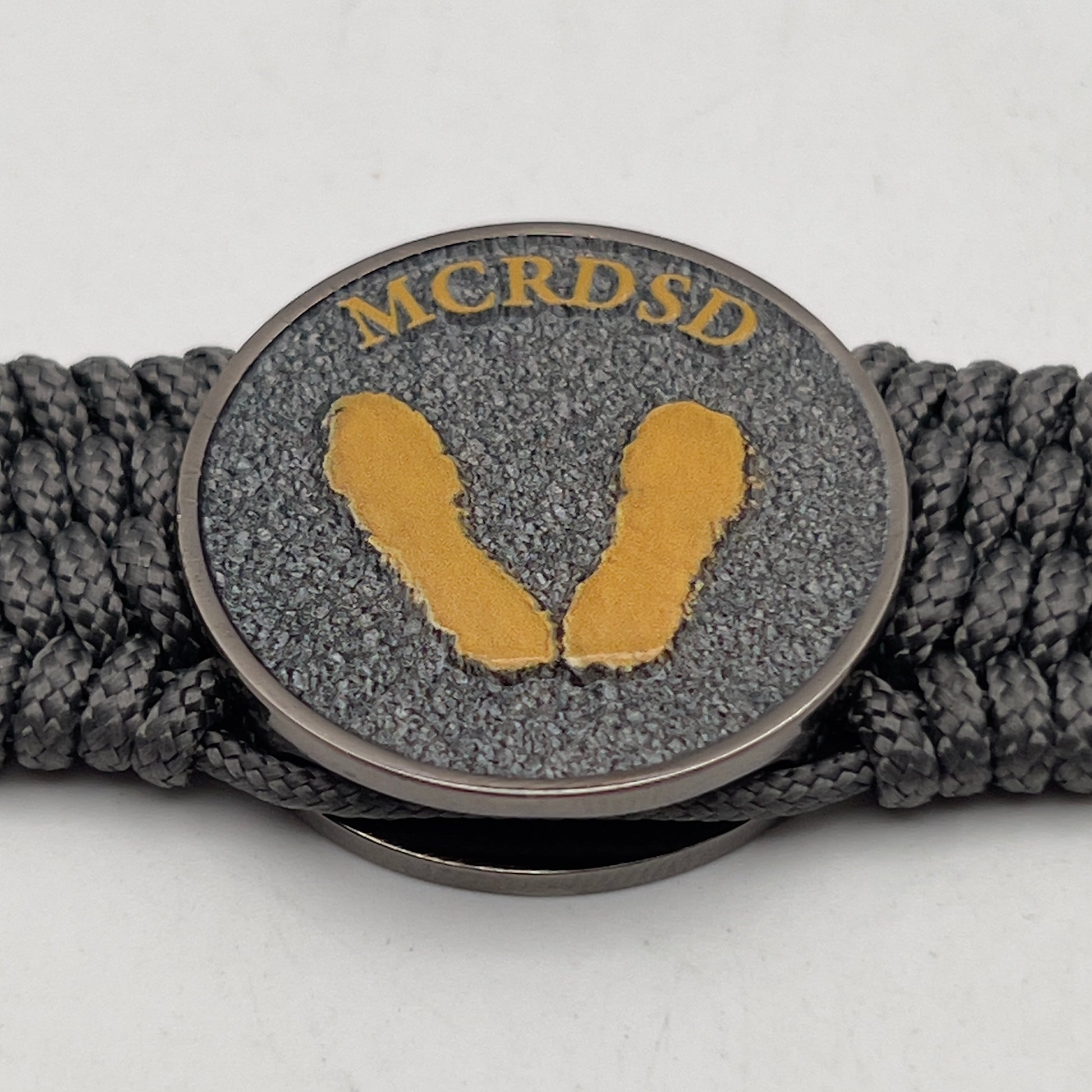 Thin, wide, flexible and comfortable braided United States Marine Corps Recruit Depot Yellow Footprints bracelet featuring a black nickel plated UV enamel painted medallion replica of an actual set of USMC footprints, a silver Cobra style tactical buckle and woven with Charcoal Gray Type-1 paracord.