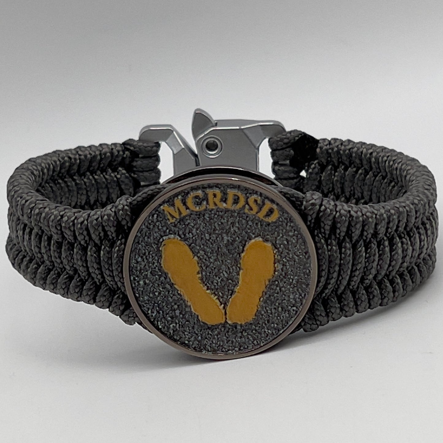 Thin, narrow, flexible and comfortable braided United States Marine Corps Recruit Depot Yellow Footprints bracelet featuring a black nickel plated UV enamel painted medallion replica of an actual set of USMC footprints, a silver Cobra style tactical buckle and woven with Charcoal Gray Type-1 paracord.
