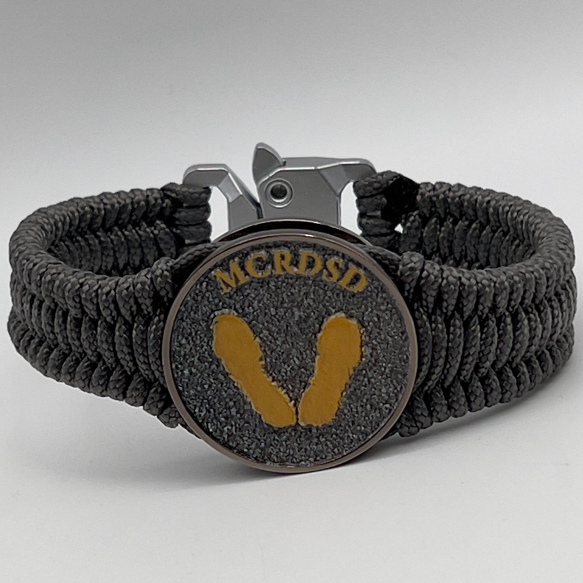 Thin, narrow, flexible and comfortable braided United States Marine Corps Recruit Depot Yellow Footprints bracelet featuring a black nickel plated UV enamel painted medallion replica of an actual set of USMC footprints, a silver Cobra style tactical buckle and woven with Charcoal Gray Type-1 paracord.